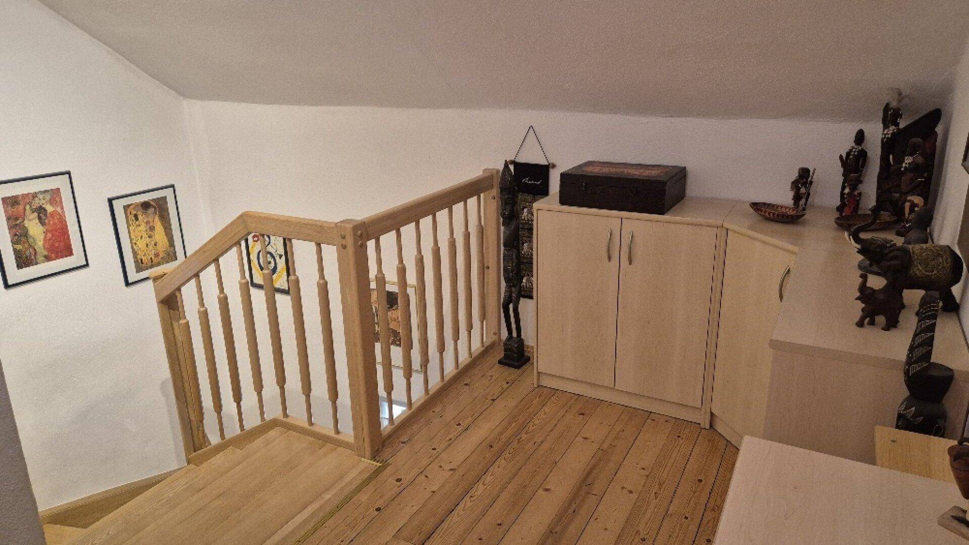 Heller Dachbodenbereich mit Holztreppe, Geländer und dekorativen Elementen, als Galerie genutzt.