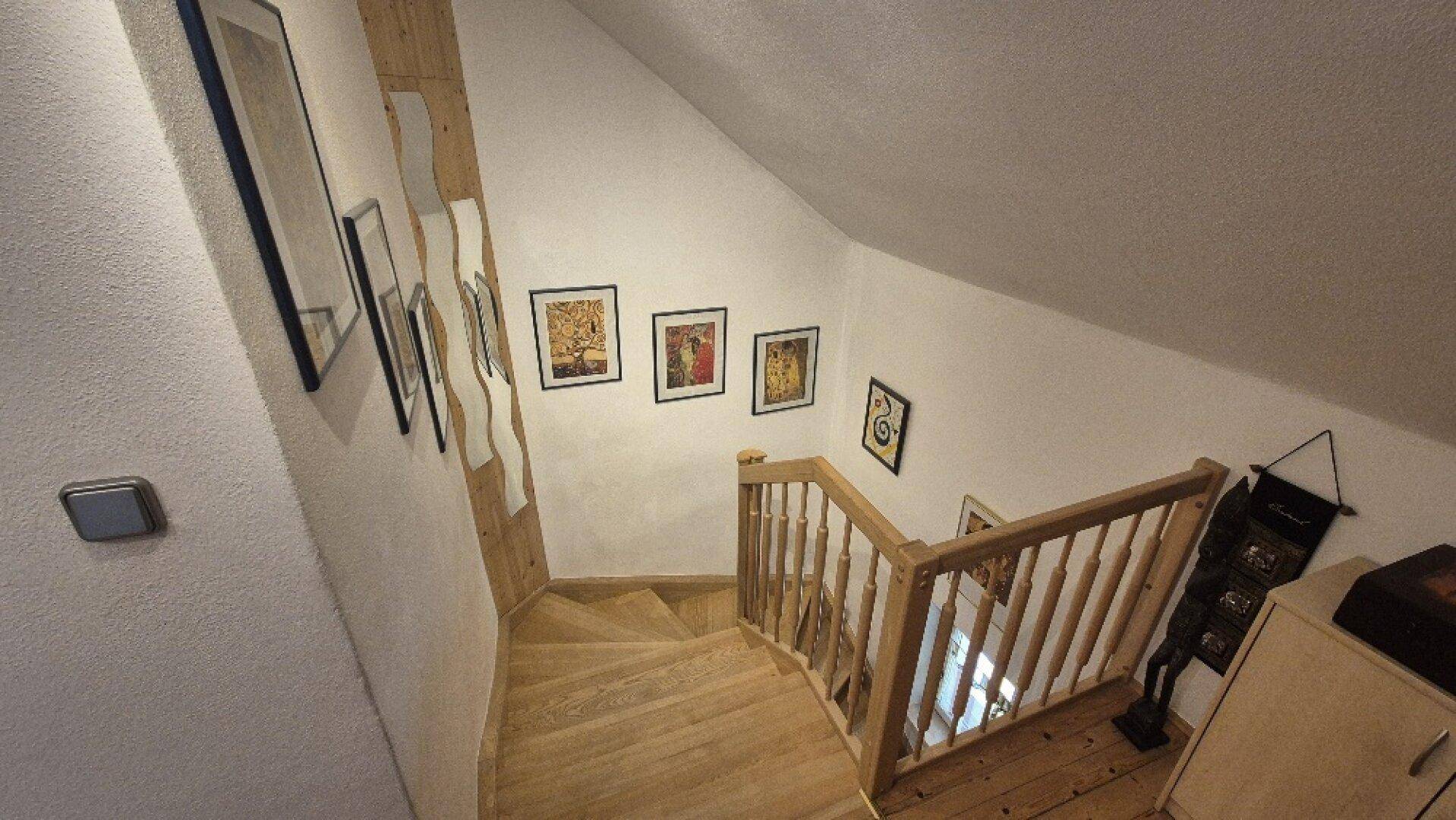 Holztreppe im Dachgeschoss mit Geländer und Kunstwerken an der Wand, führt nach unten.