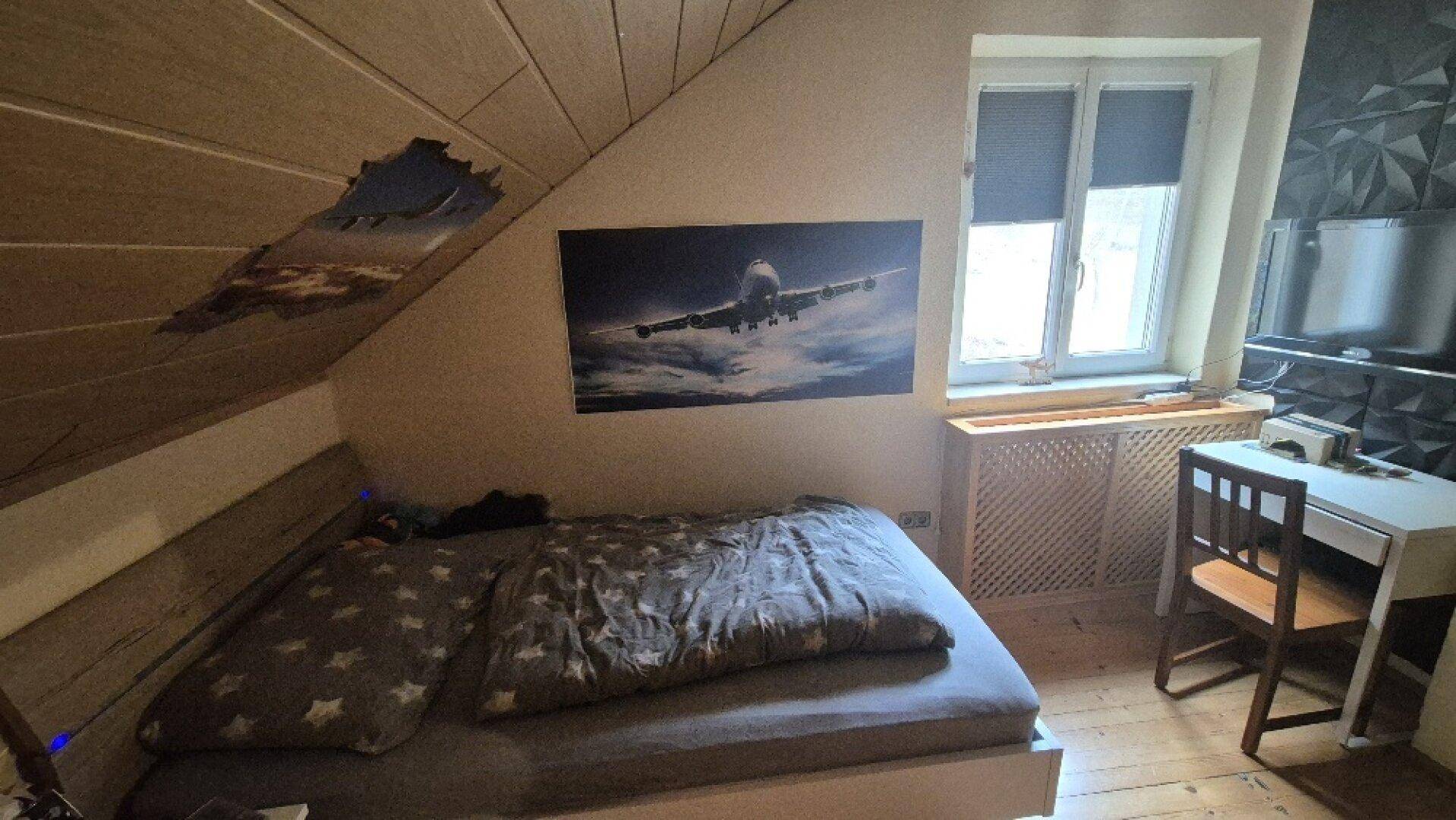 Gemütliches Schlafzimmer im Dachgeschoss mit Holzbett, Schreibtisch und Fenster mit Blick ins Grüne.
