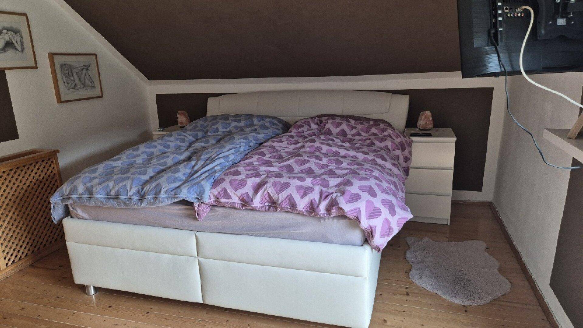 Schlafzimmer im Dachgeschoss mit Doppelbett, Nachttischen und schrägen Wänden, gemütlich eingerichtet.