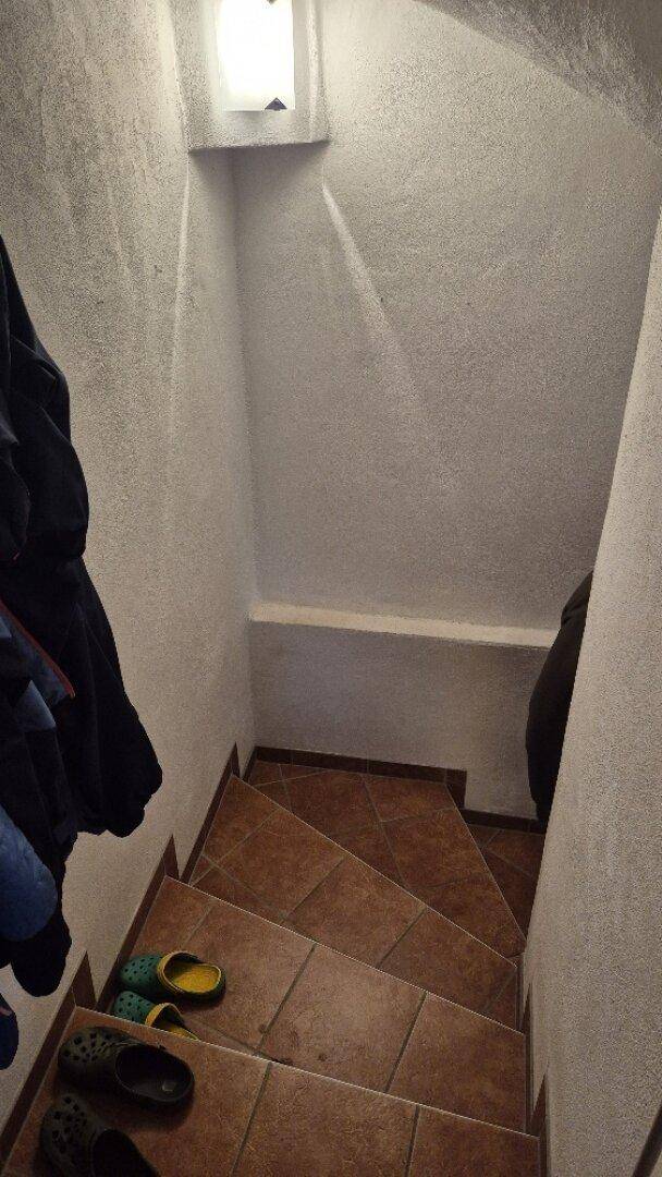 Geflieste Treppe mit braunen Fliesen und weiß gestrichenen Wänden, führt in ein Untergeschoss.