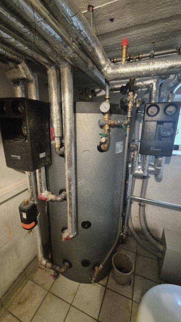 Großer Warmwasserspeicher mit Rohrleitungen und Messgeräten, Teil der Heizungsanlage.