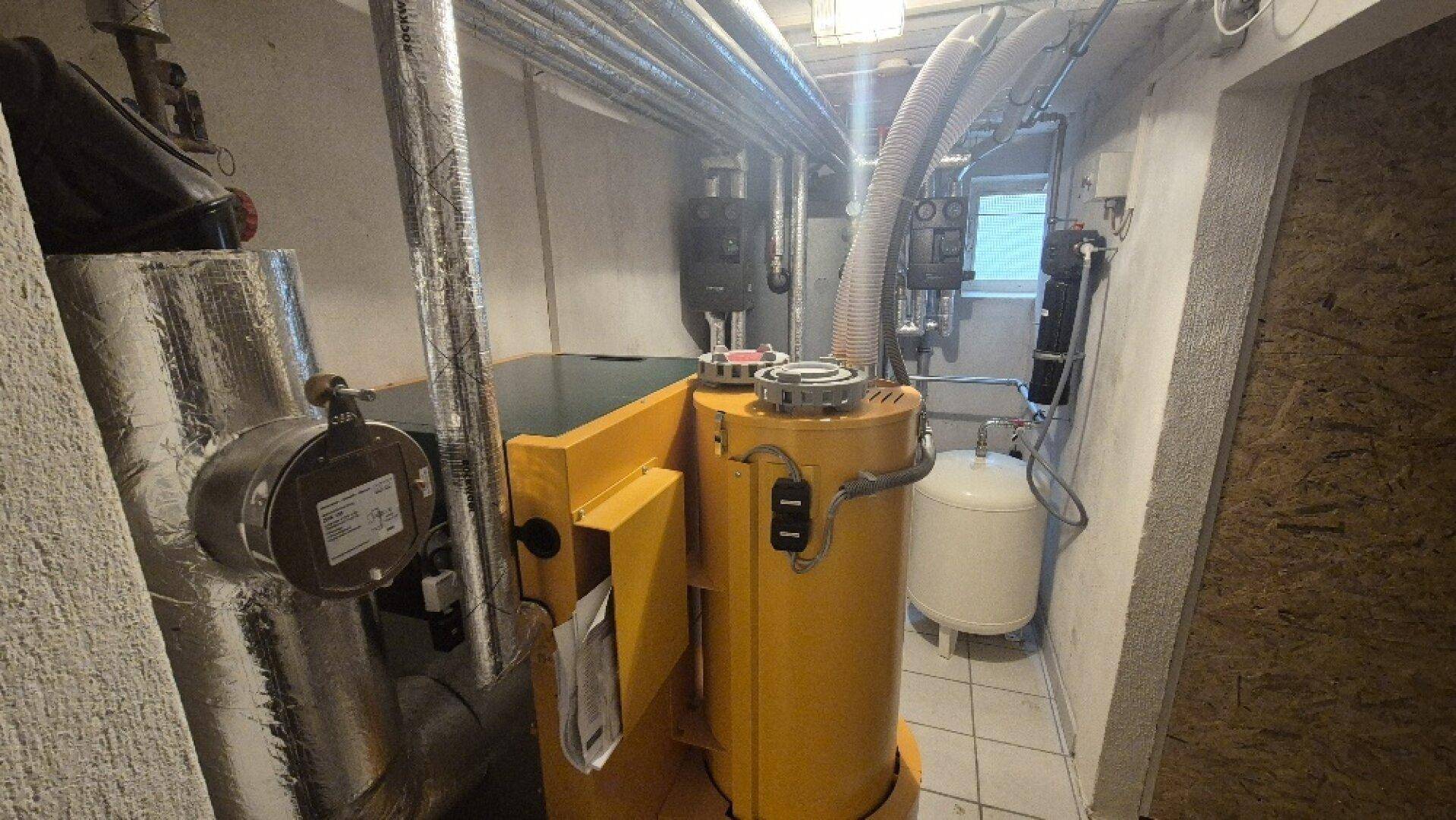 Heizungsanlage mit gelbem Kessel und isolierten Rohren, sorgt für Wärme im gesamten Gebäude.
