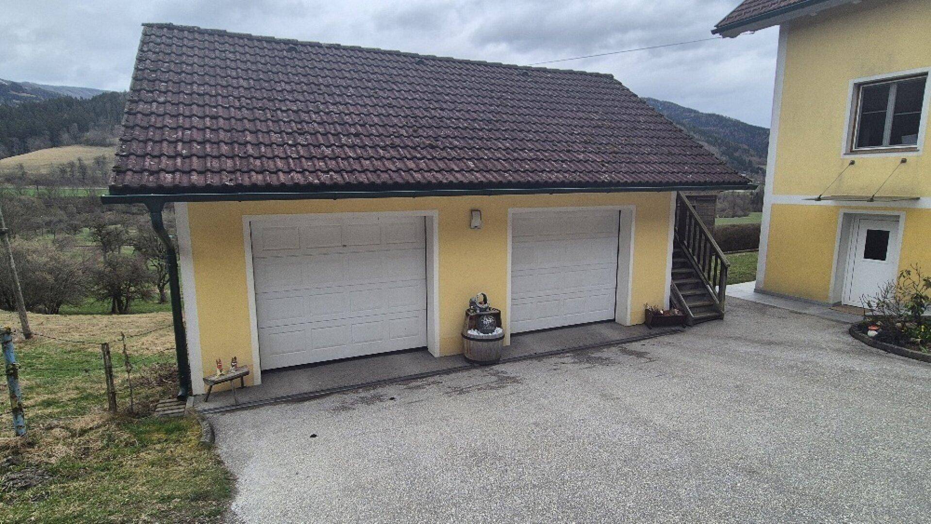 Freistehende Doppelgarage mit zwei weißen Toren und Satteldach neben dem Wohnhaus.