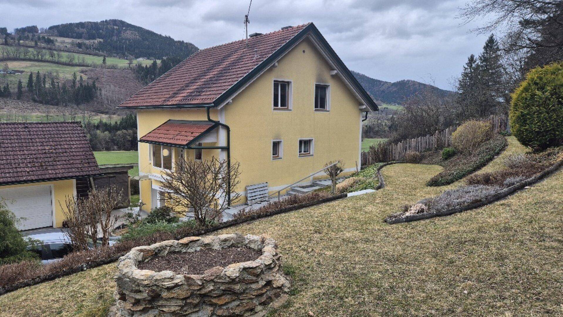 Gelbes Einfamilienhaus mit großem Garten und Blick auf die umliegende Hügellandschaft.
