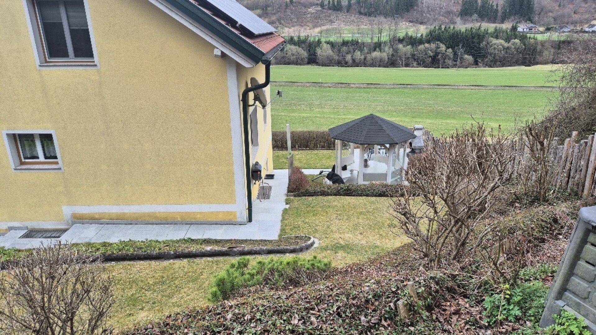 Weitläufiger Gartenbereich neben dem Haus mit Rasenfläche und weitem Blick über grüne Felder.