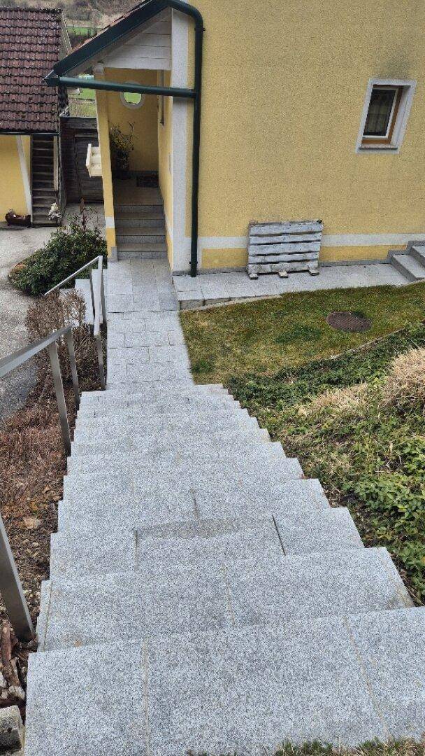 Außentreppe aus grauen Fliesen mit Metallgeländer, die zum Eingang des Hauses führt.