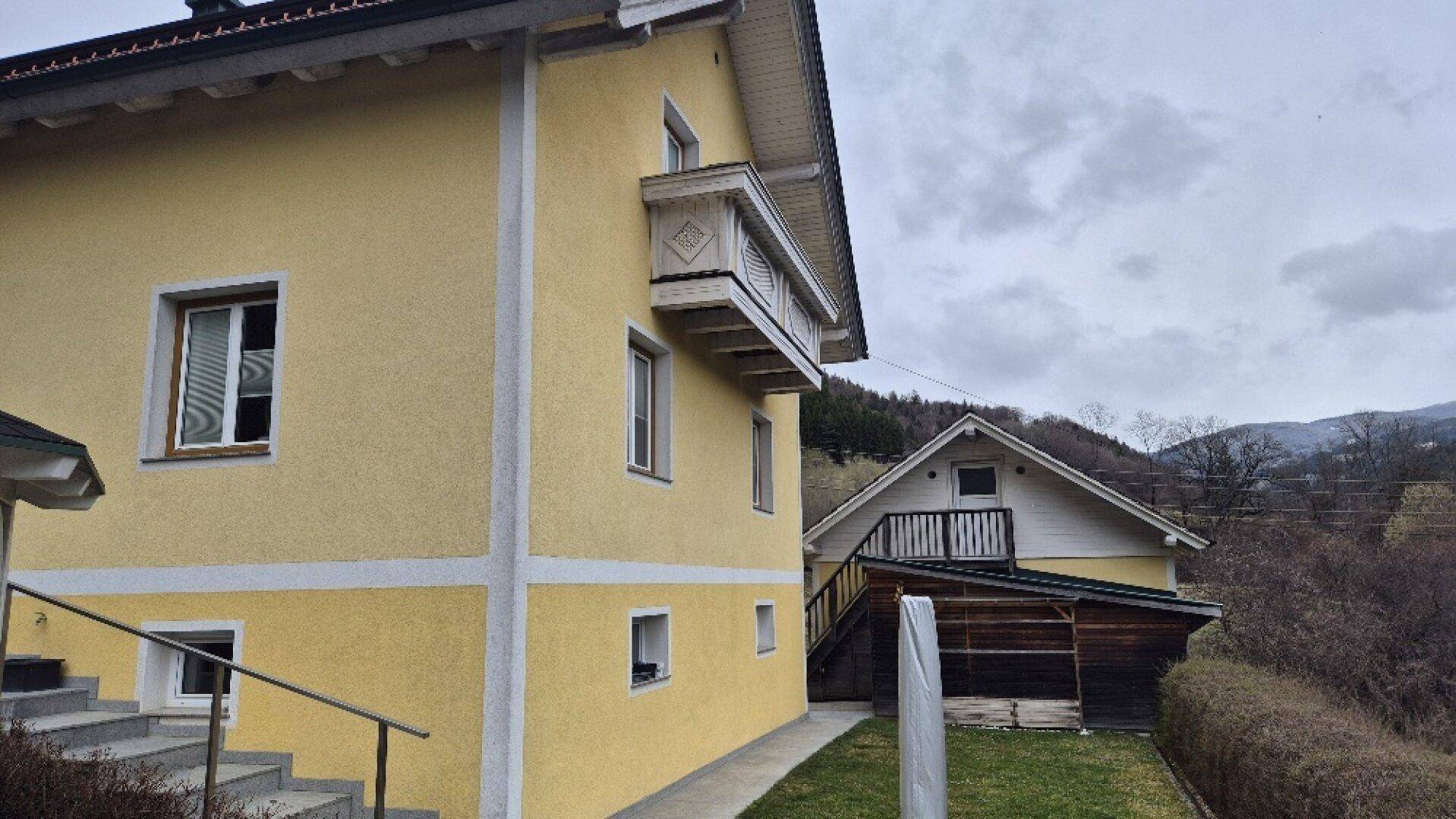 Seitenansicht des Hauses mit einem kleinen, traditionellen Holzbalkon und Blick ins Grüne.