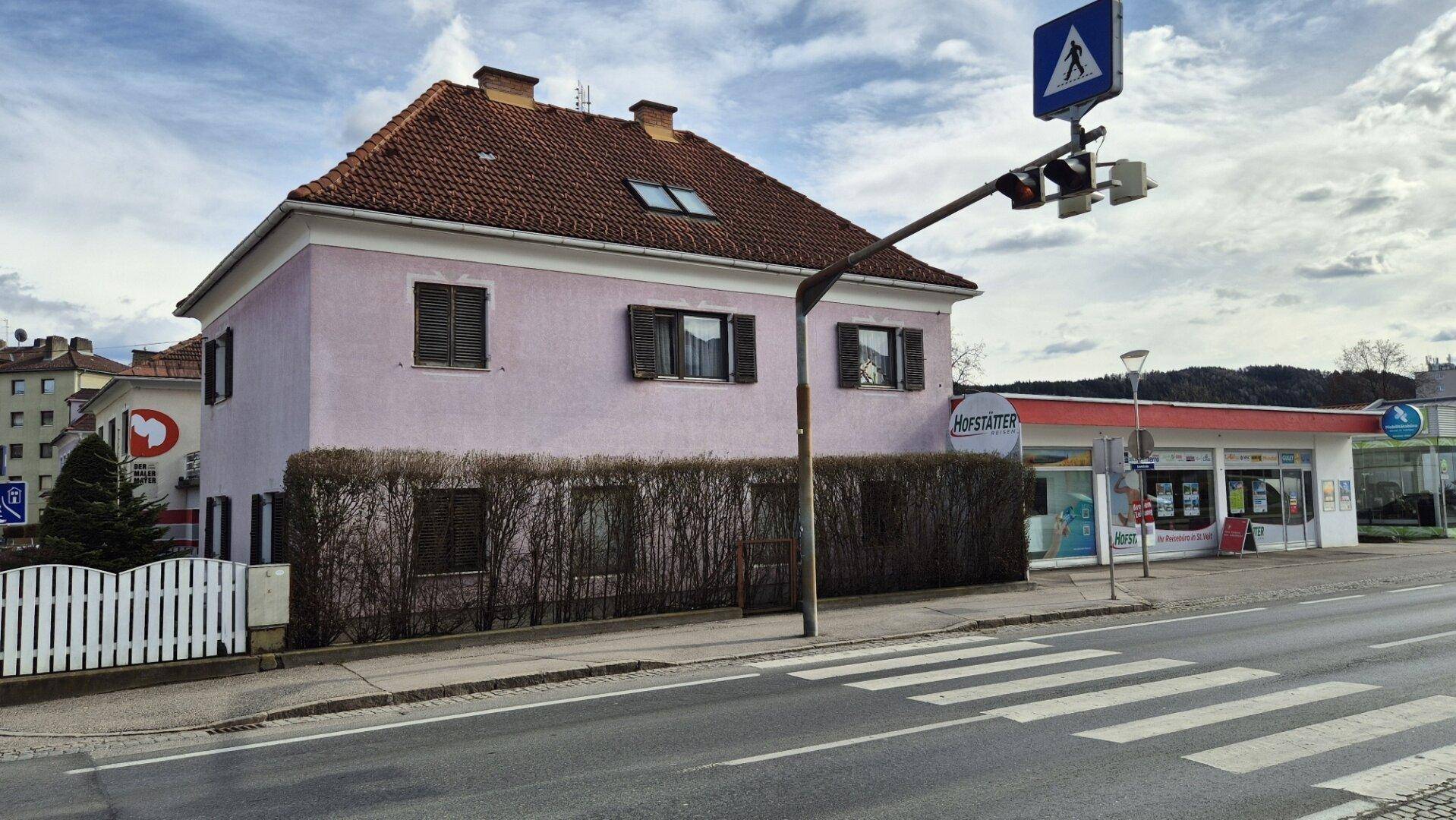 Gebäudeansicht von der Straßenseite mit Fußgängerüberweg und angrenzendem Gewerbeobjekt.