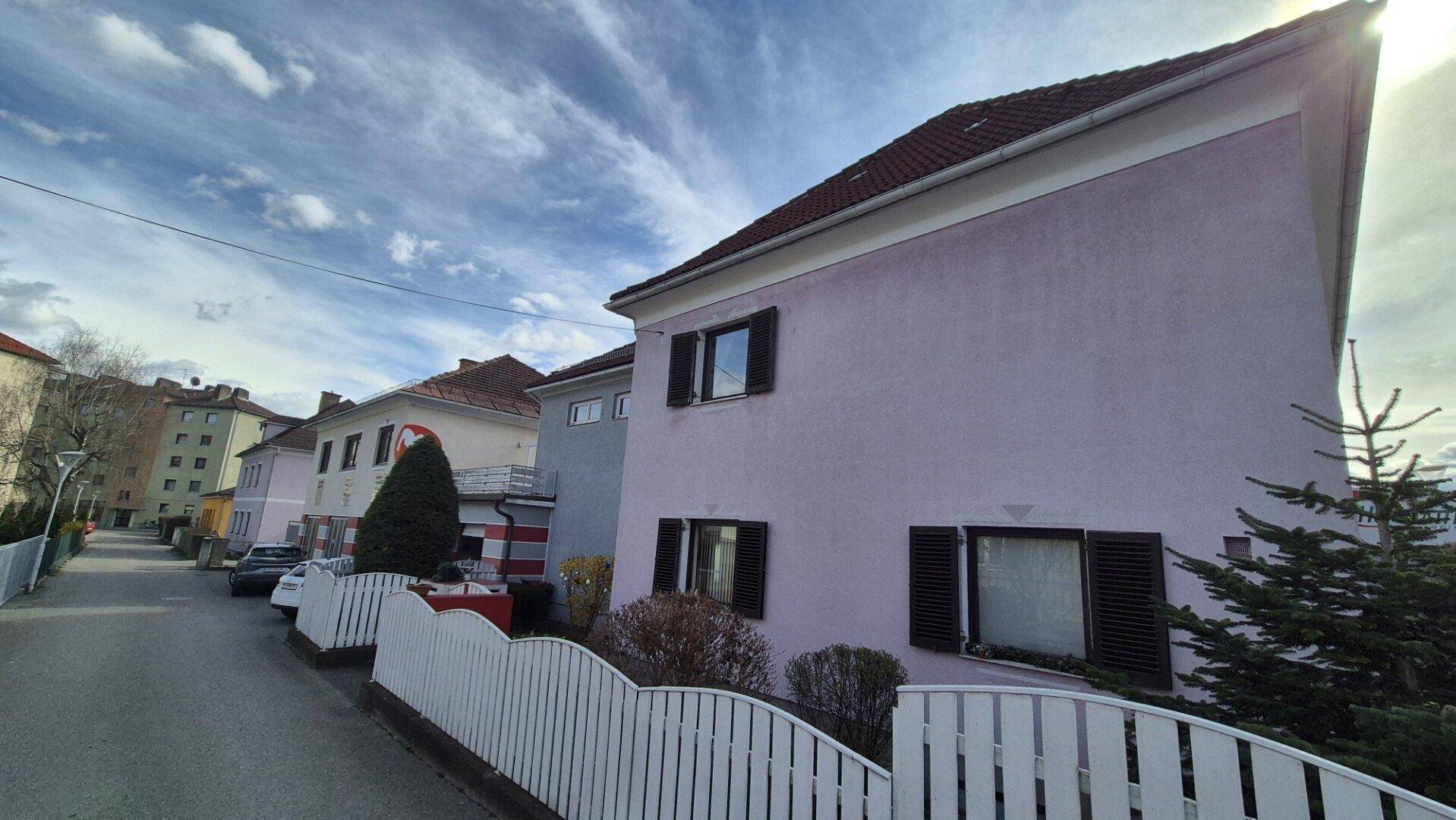 Seitenansicht des Wohnhauses mit weißem Zaun und weiteren Gebäuden in der Nachbarschaft.