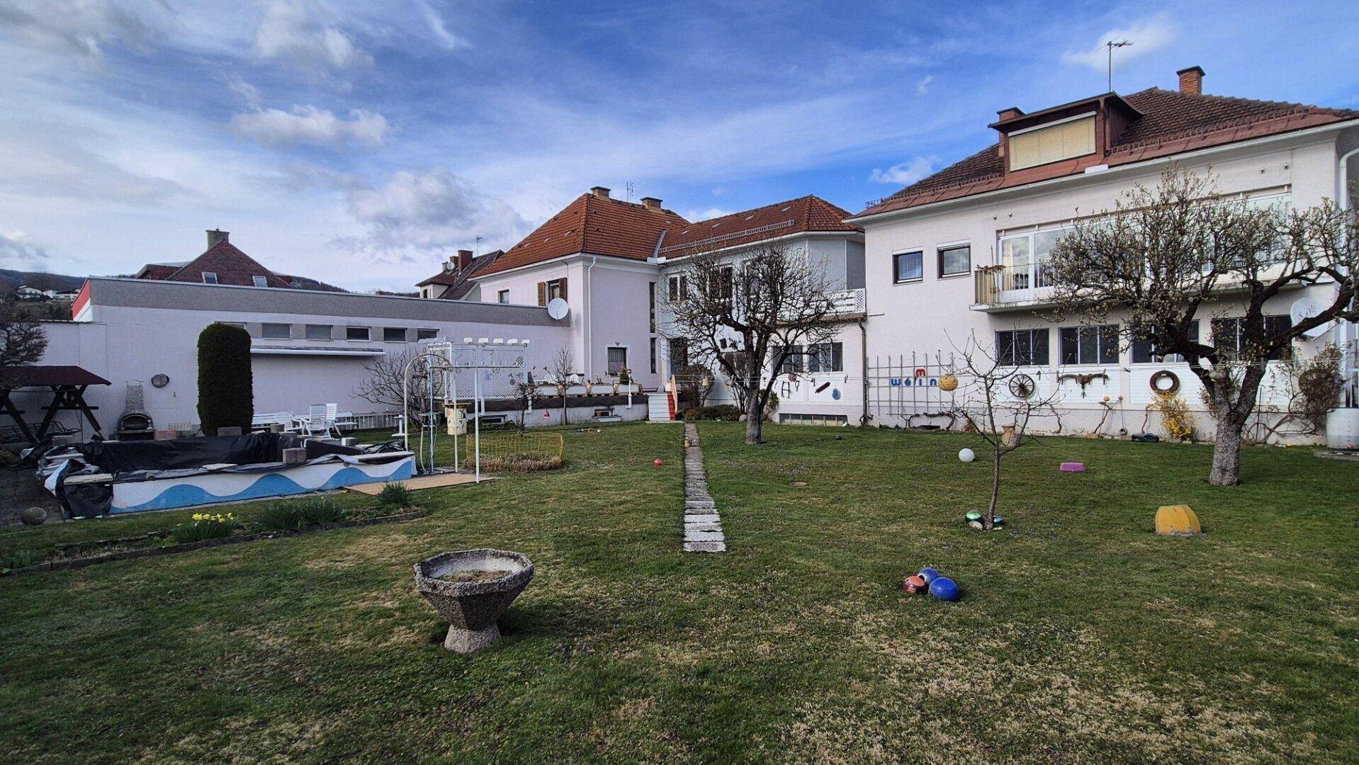 Weitläufiger Gartenbereich mit Rasen, Bäumen und Blick auf die Rückseite des Wohnhauses.
