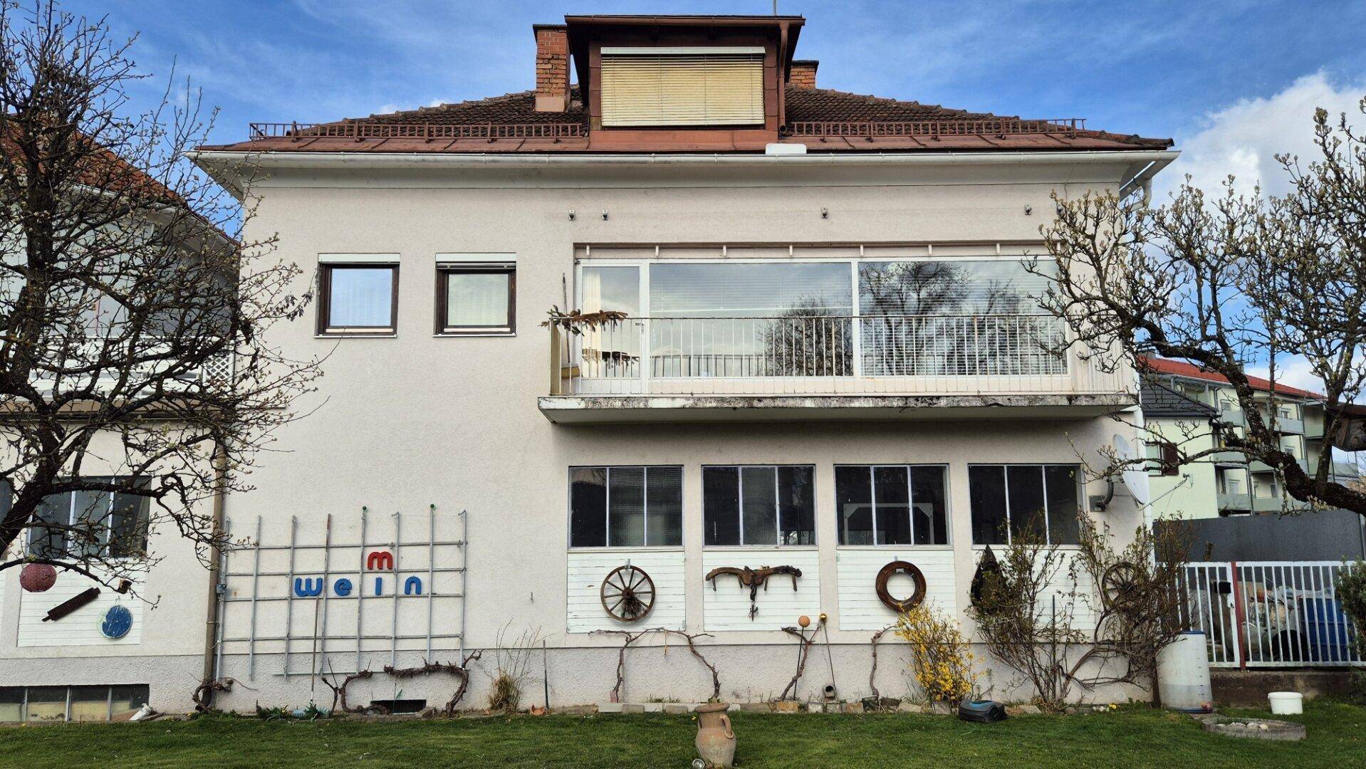 Rückfassade des Hauses mit großem verglastem Balkon und dekorativen Elementen im Garten.