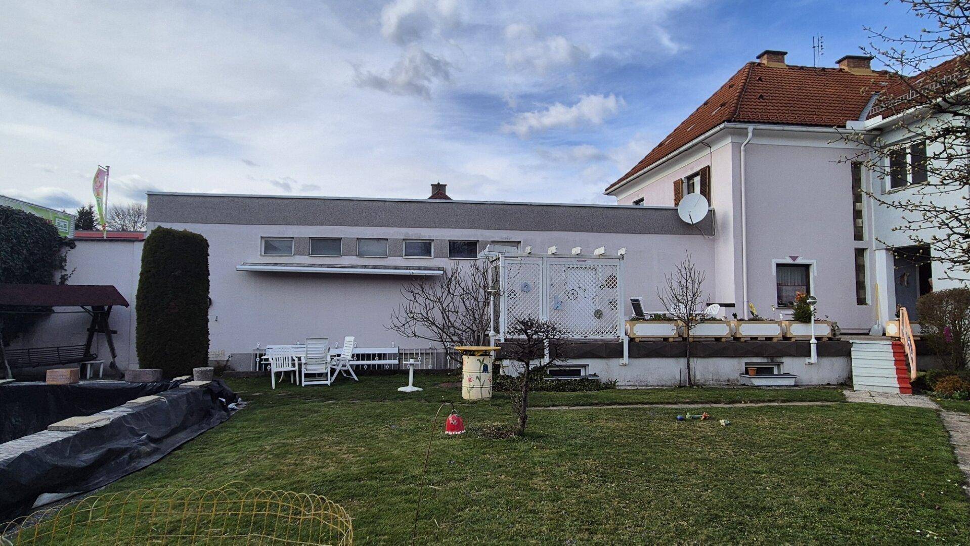 Hinteransicht des Anwesens mit Garten, Sitzbereich und einem Anbau mit Flachdach.