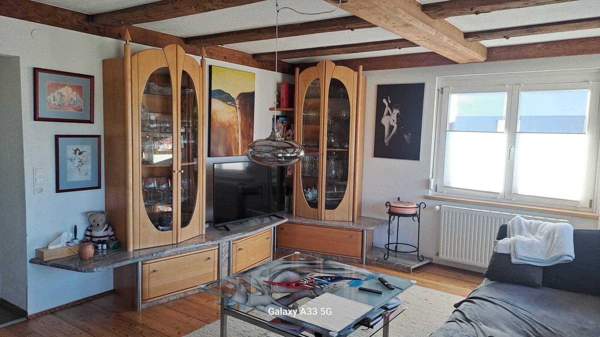 Wohnzimmer mit Holzbalken an der Decke, Vitrinen und einem Couchtisch aus Glas.