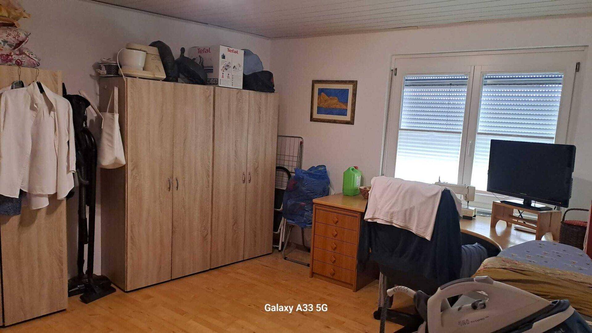 Schlafzimmer mit Kleiderschränken, Bügelbrett und einem Fenster mit Jalousien.