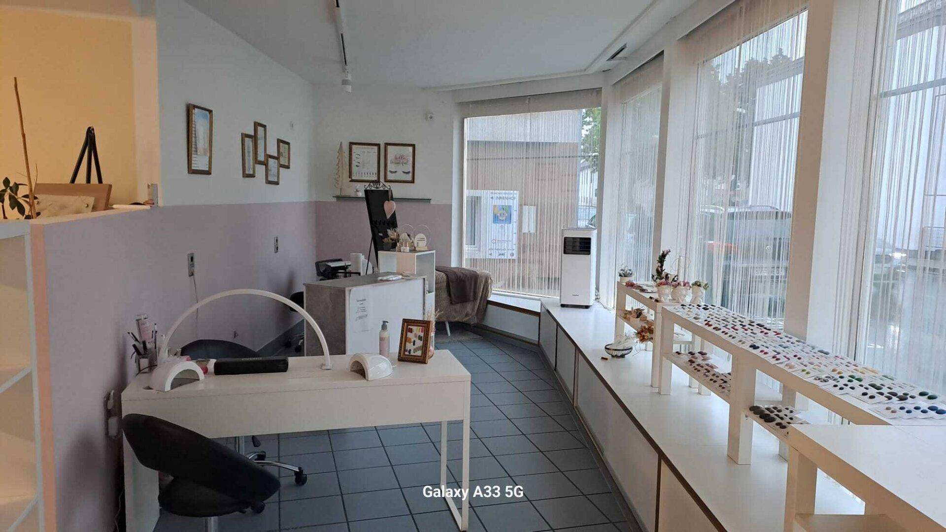 Heller Raum, möglicherweise ein Nagelstudio, mit großen Fenstern und Arbeitsplätzen.