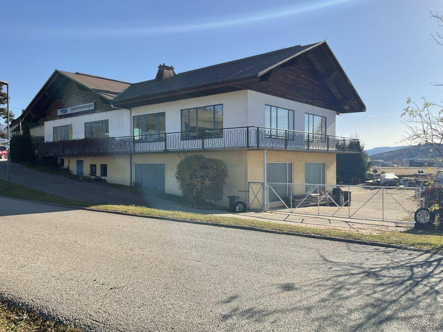 Seitenansicht des Gewerbegebäudes mit Balkon und großen Fensterfronten, umgeben von einer Zufahrt.