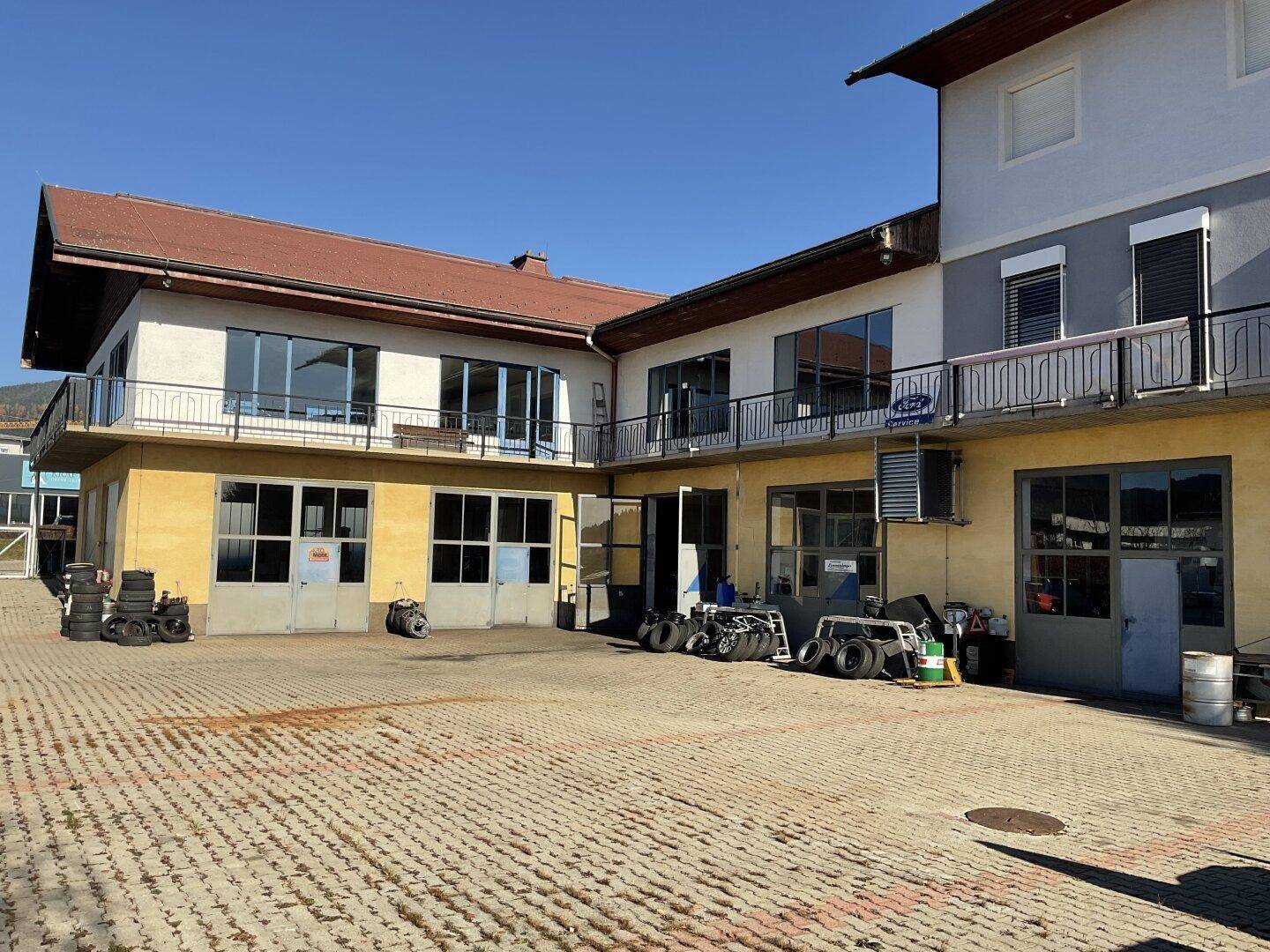 Gepflasterter Innenhof zwischen den Gebäudeteilen mit Lagerflächen und Fahrzeugen im Freien.