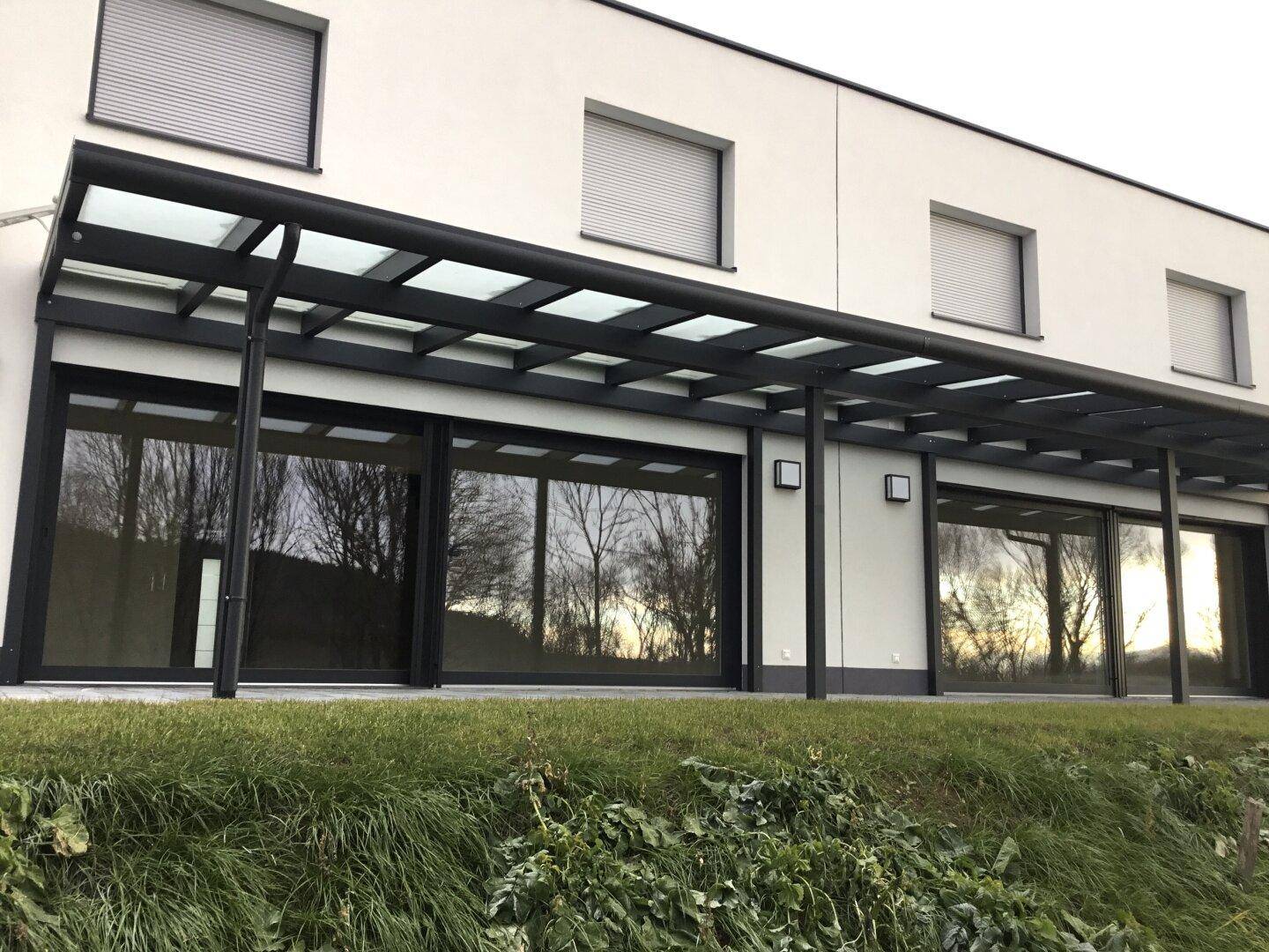 Überdachte Terrasse mit großen Glasfronten und Blick ins Grüne, ideal für entspannte Stunden im Freien.