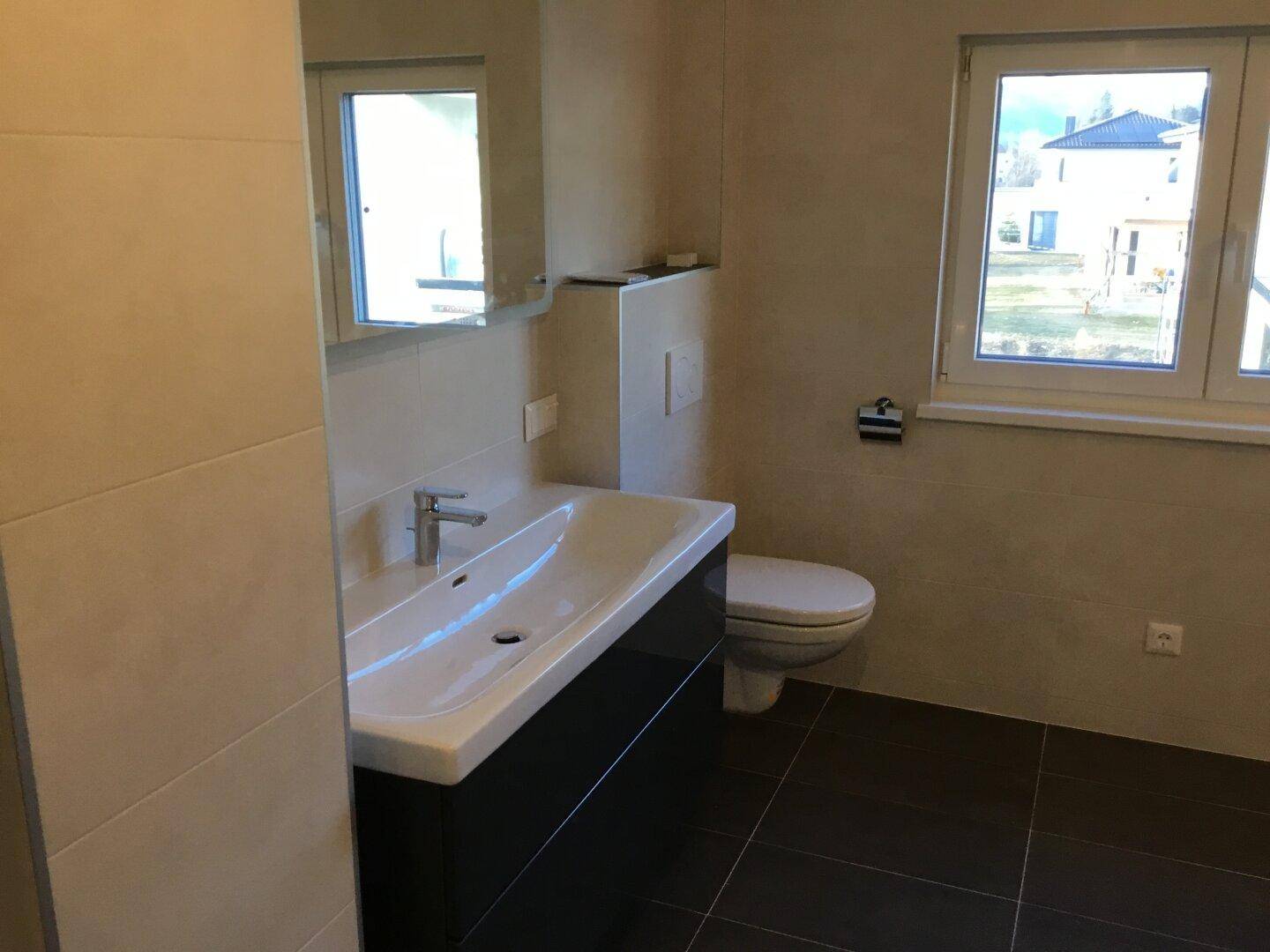 Modernes Badezimmer mit großem Waschbecken, WC und Fenster, ausgestattet mit hellen Fliesen.