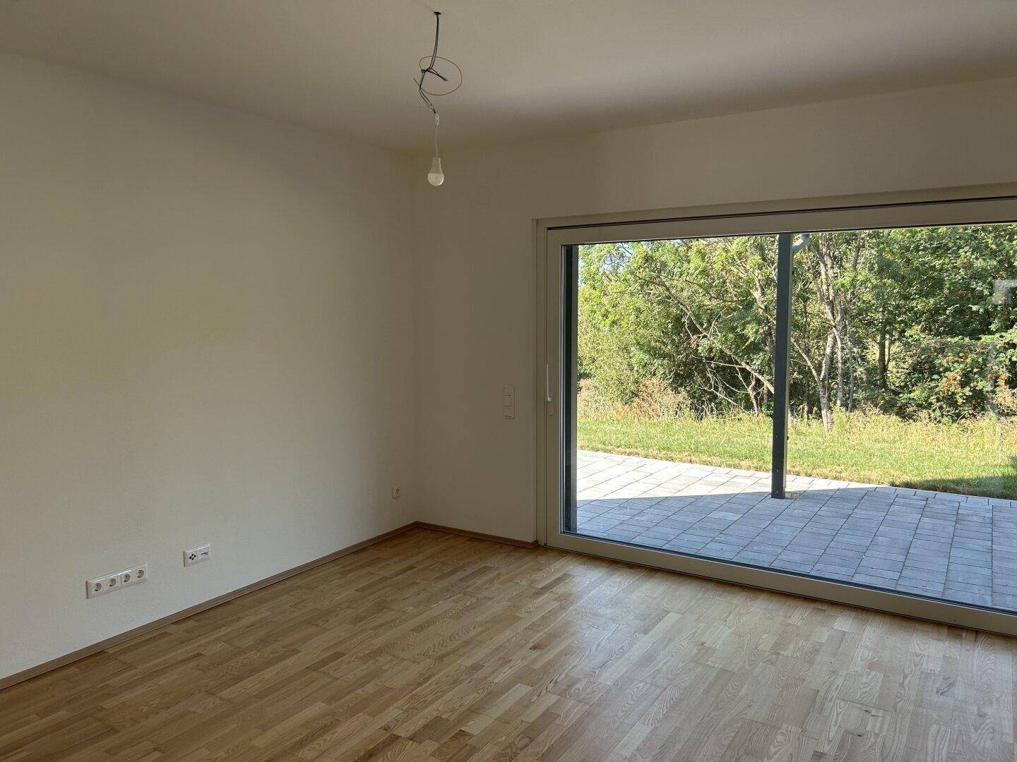 Heller Wohnbereich mit Holzboden und großer Schiebetür zur Terrasse, die viel Tageslicht hereinlässt.