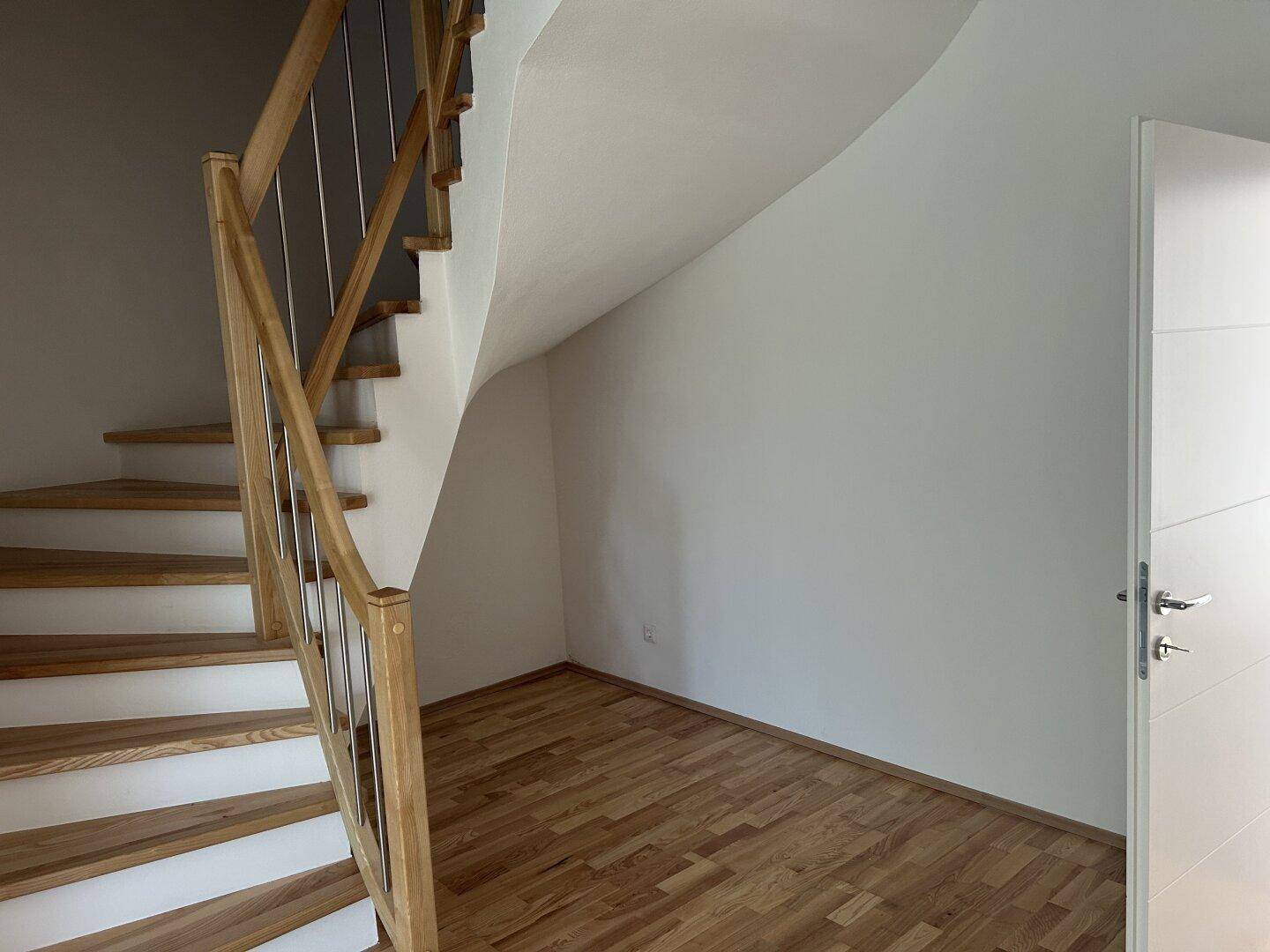 Heller Flur mit moderner Holztreppe und passendem Holzboden, der zu den oberen Etagen führt.