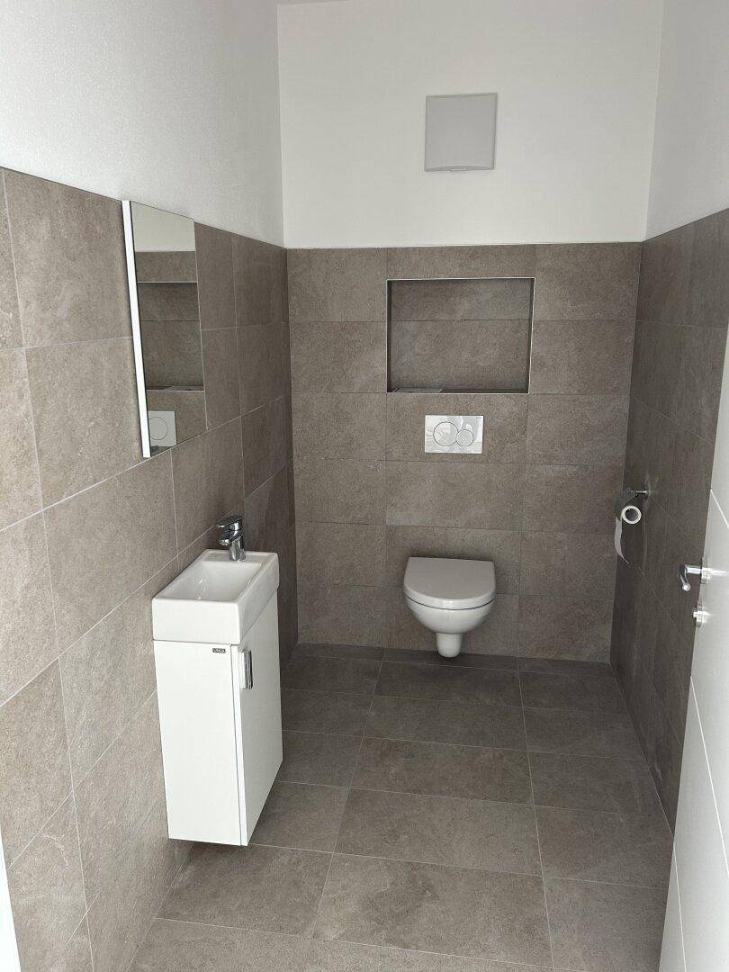 Kleines Gäste-WC mit modernem Design, Wand-WC und Handwaschbecken, komplett gefliest.