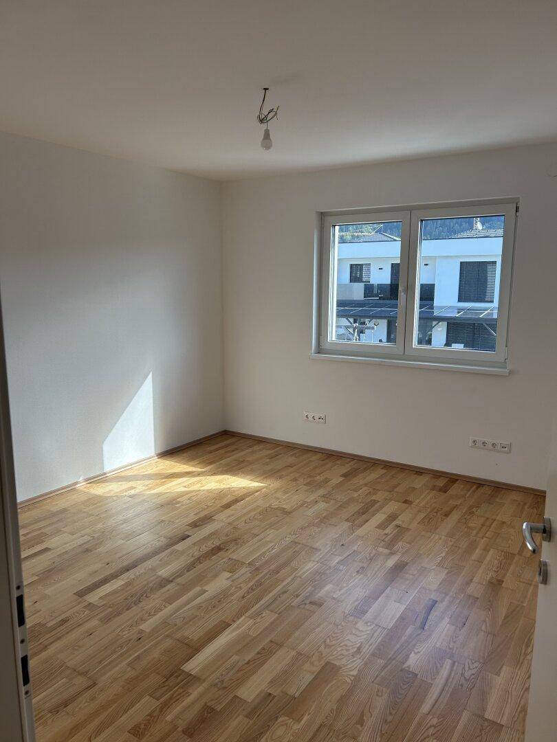 Helles Schlafzimmer mit Holzboden und Fenster, das einen Blick auf die umliegenden Häuser bietet.