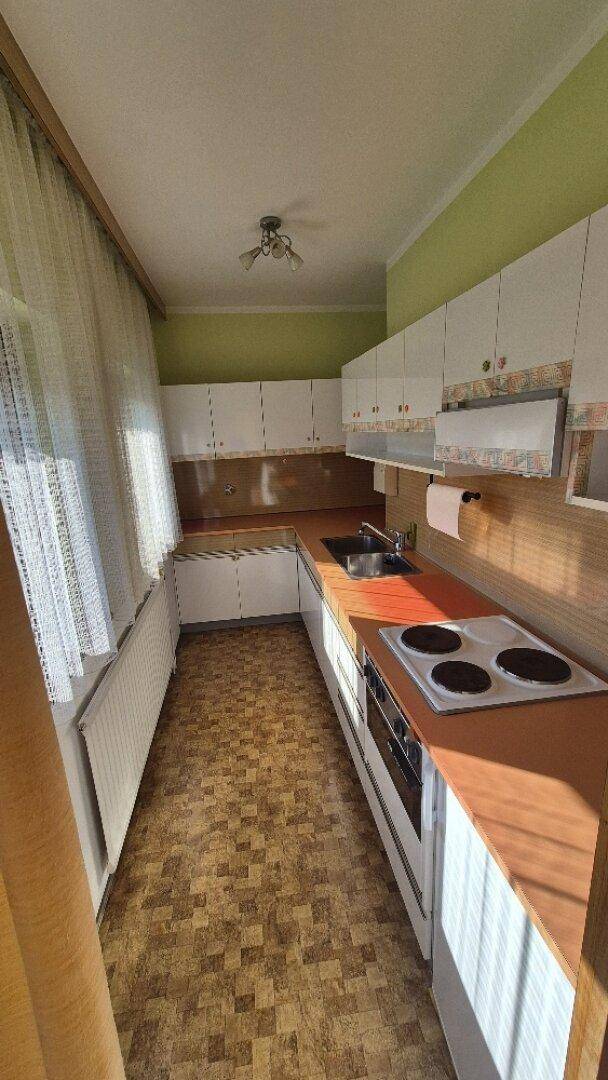 Schmale Küche mit älteren Einbaumöbeln, Fenster und Linoleumboden, funktional und hell.