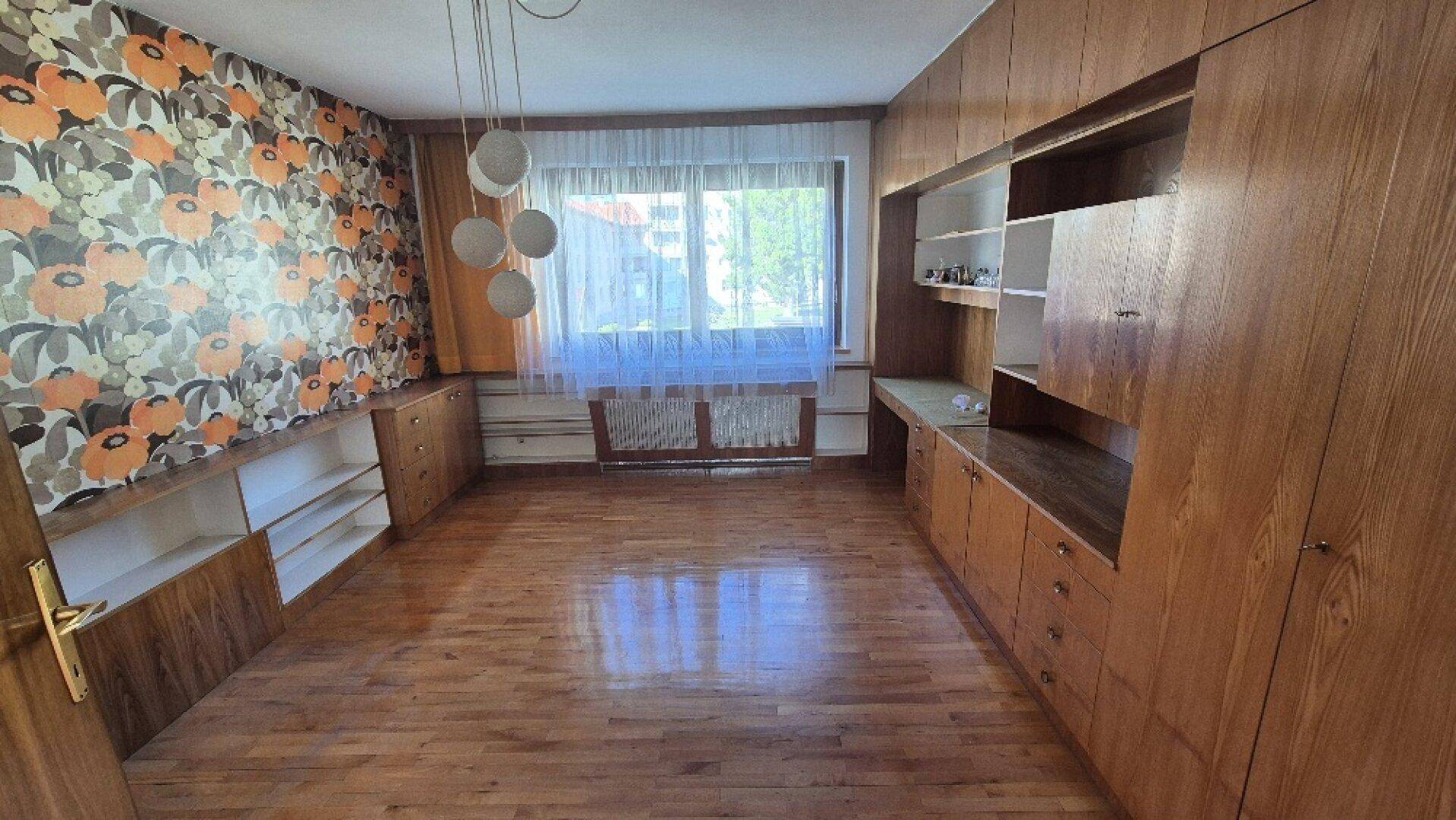 Schlafzimmer mit Holzschränken, floraler Tapete und Parkettboden, bietet viel Stauraum.
