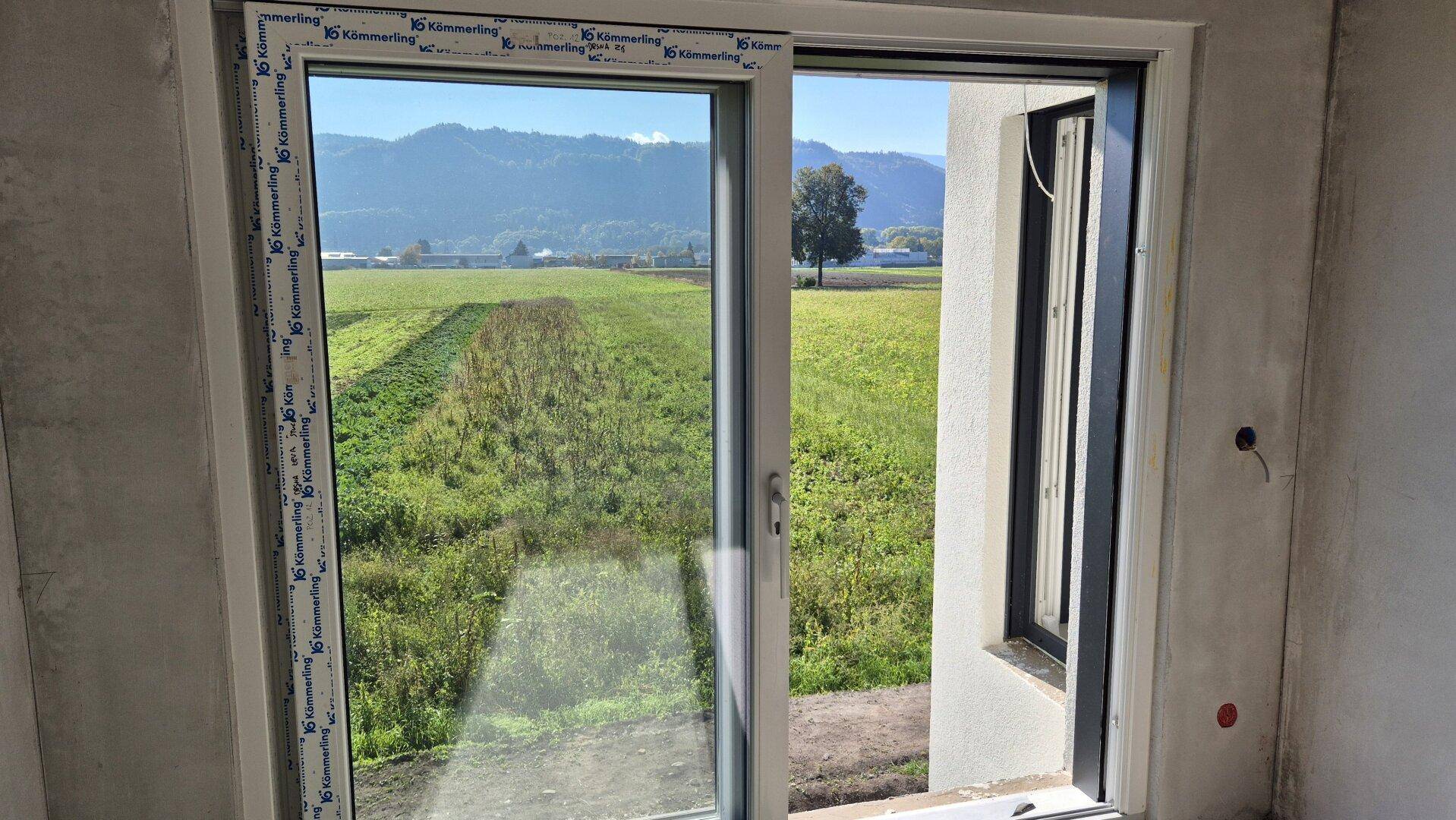 Innenraum im Rohbau mit Schiebetür und weitem Ausblick auf die ländliche Umgebung.
