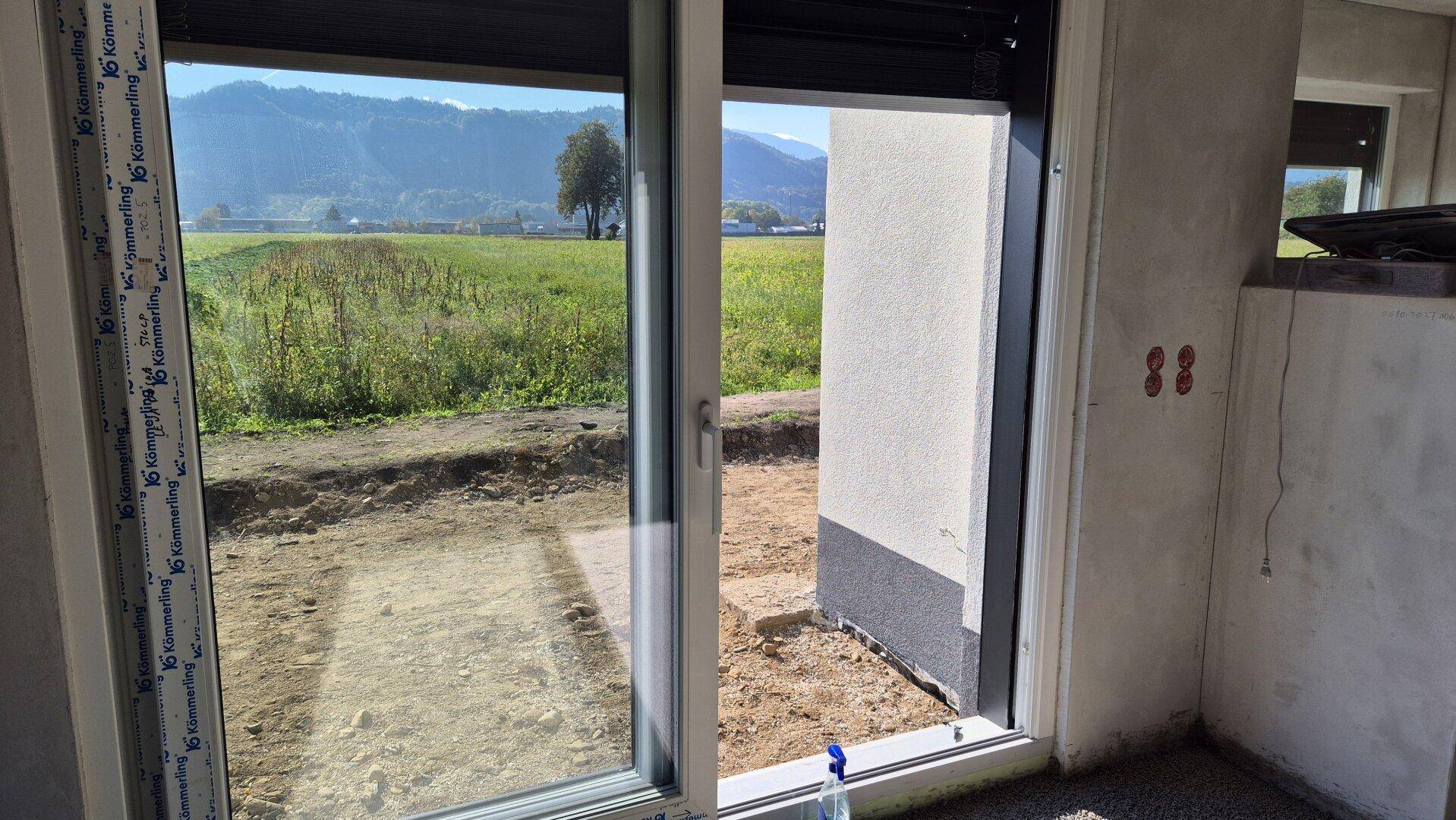 Unfertiger Raum mit Schiebetür und Blick auf die grüne Landschaft und die Berge.