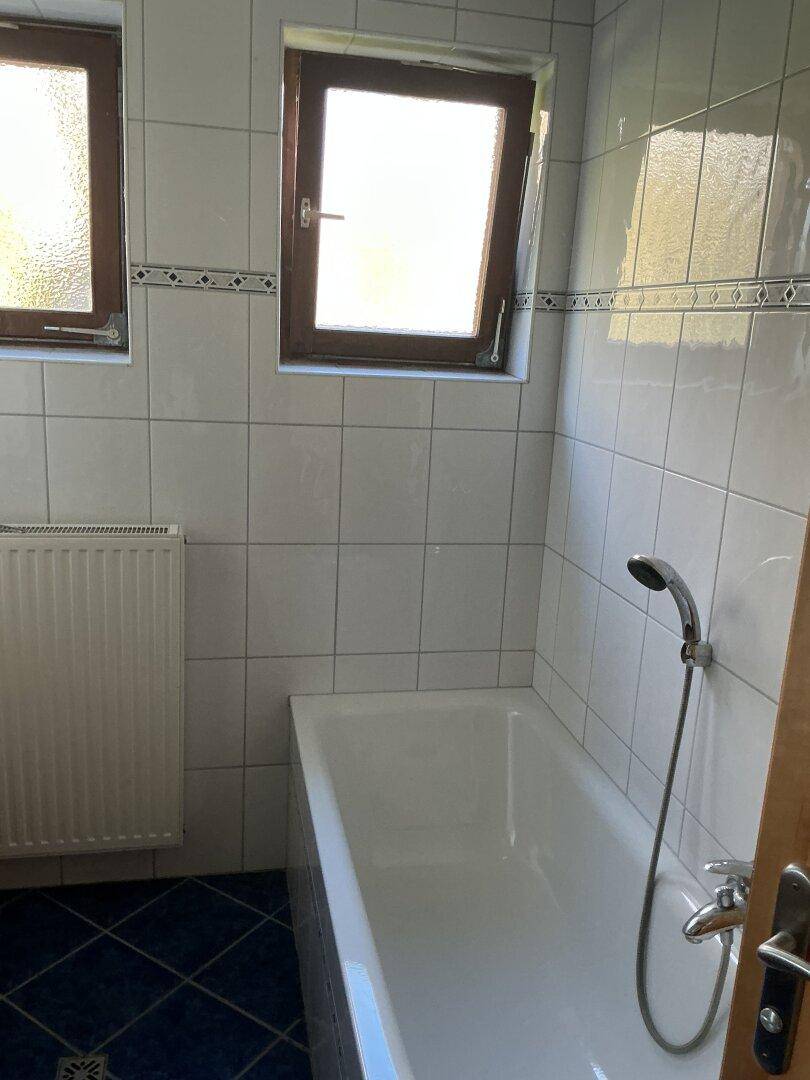 Badezimmer mit Badewanne, Fenster und weiß gefliesten Wänden.
