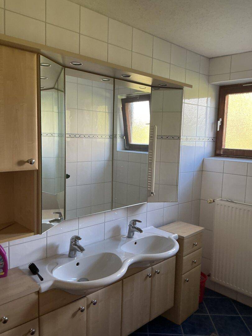 Helles Badezimmer mit Doppelwaschbecken, großem Spiegelschrank und Fenster.