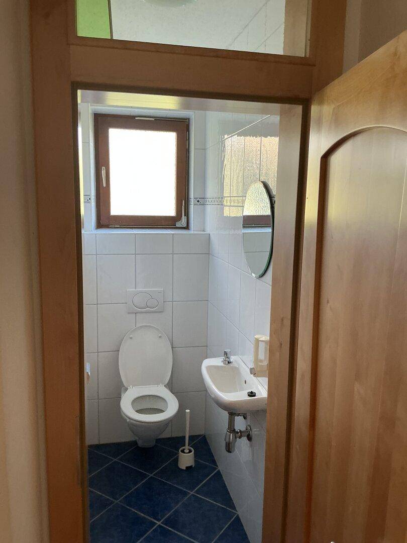 Kleines Gäste-WC mit Fenster, weiß gefliesten Wänden und blauem Boden.