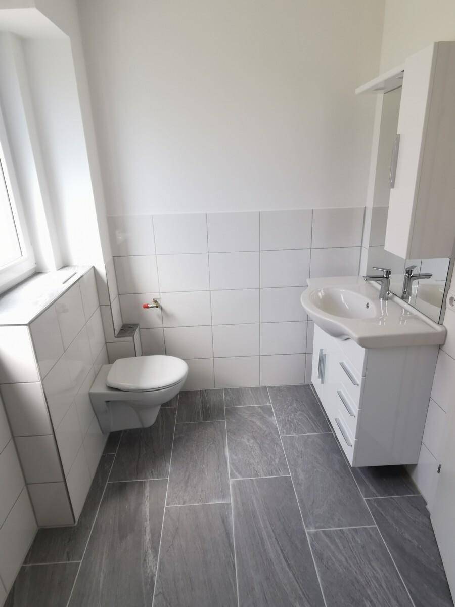 Modernes Badezimmer mit WC, Waschbecken, Spiegelschrank und grauen Fliesen.