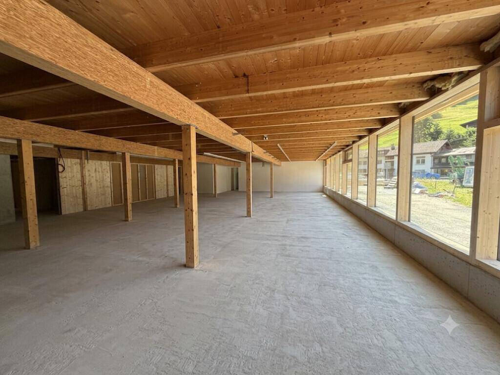 Großer, offener Innenraum mit Holzbalkendecke, Betonboden und vielen Fenstern, ideal für Gewerbe.