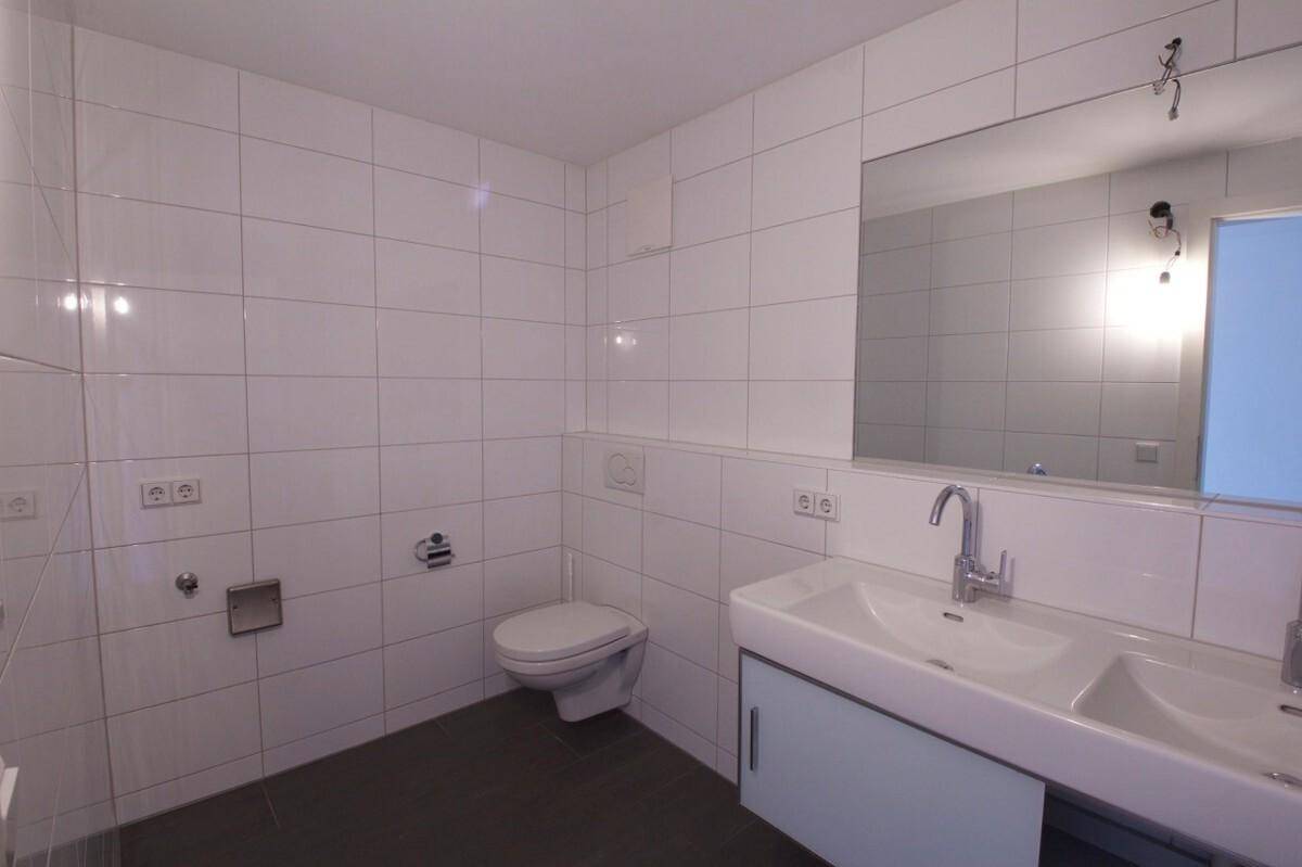 Modernes Badezimmer mit weißen Fliesen, dunklem Boden, Doppelwaschbecken und Wand-WC.