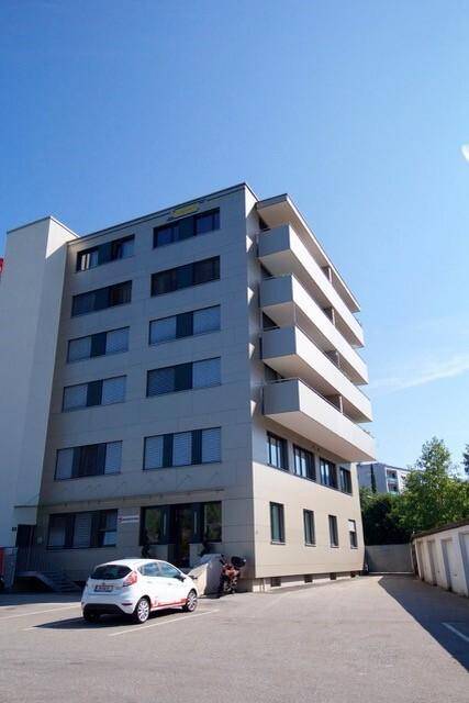 Modernes Apartmentgebäude mit mehreren Etagen und Balkonen unter blauem Himmel.