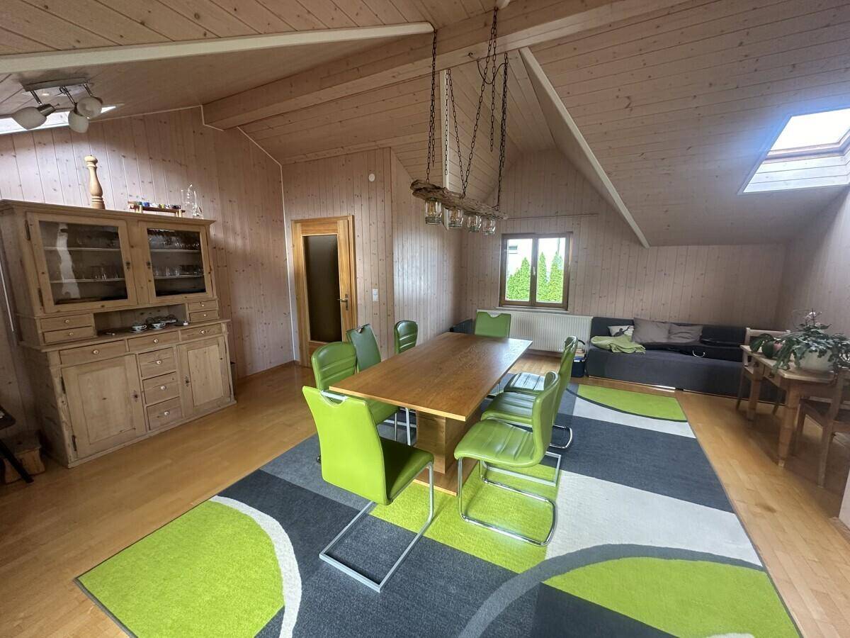 Geräumiger Wohn-Essbereich mit Holztisch, grünen Stühlen und Holzdeckenverkleidung.