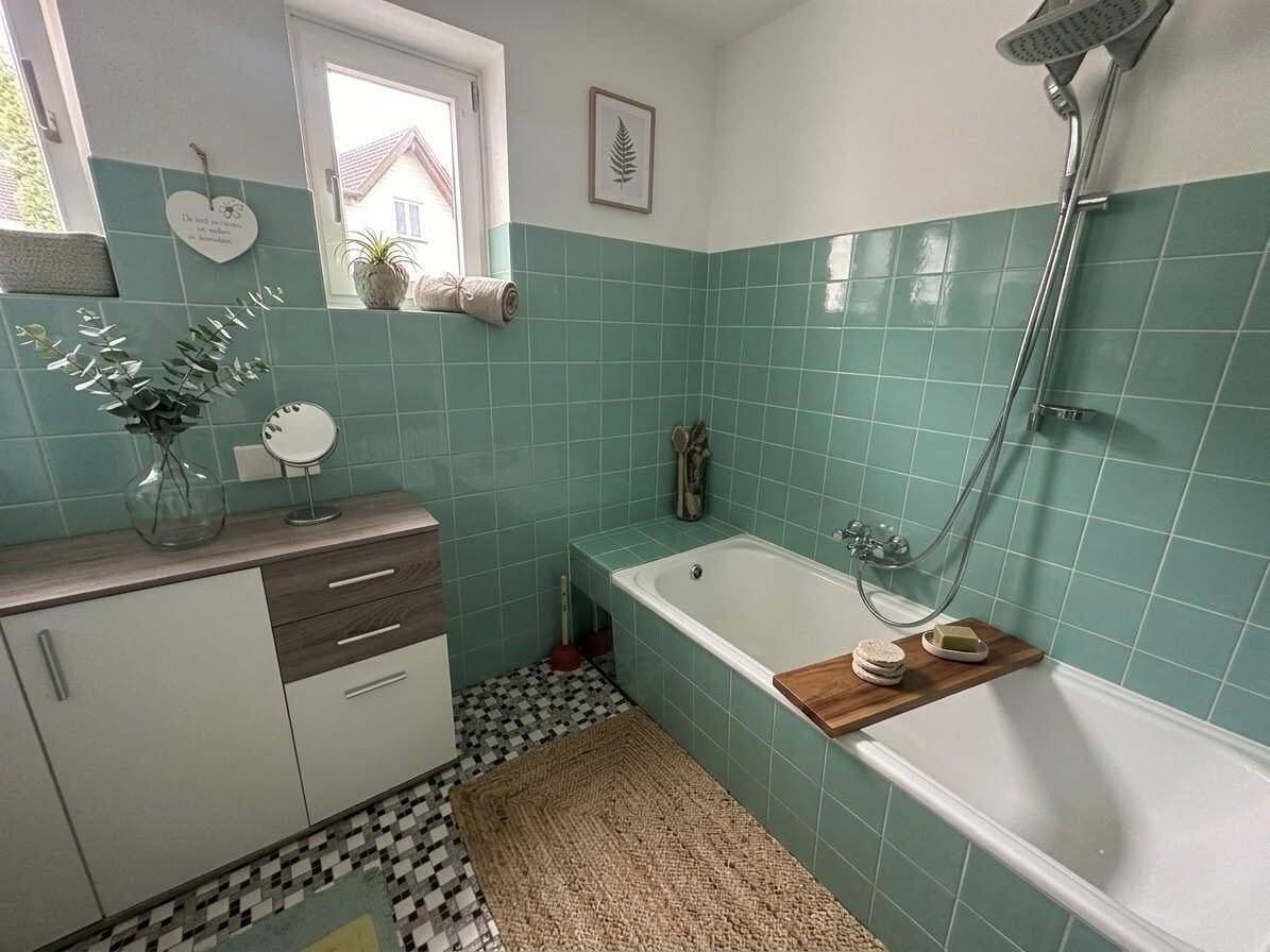 Badezimmer mit grünen Fliesen, Badewanne und Fenster für Tageslicht.