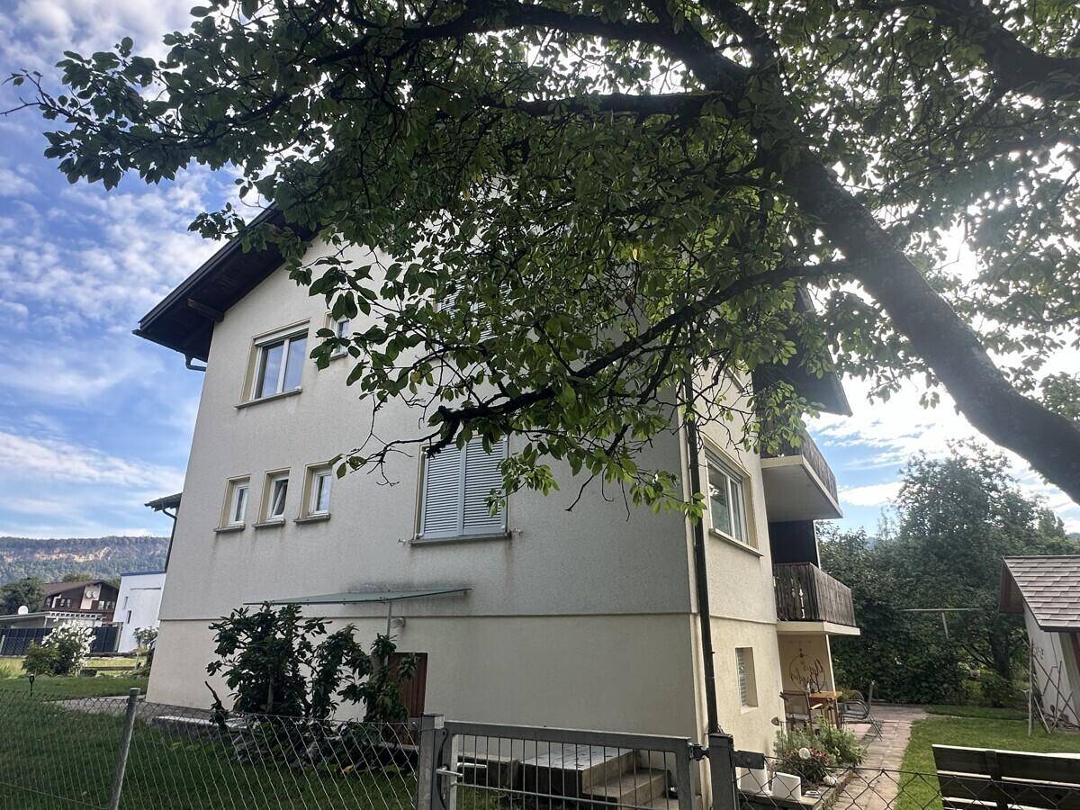 Seitenansicht des Hauses mit Balkonen und Fenstern, umgeben von Bäumen.