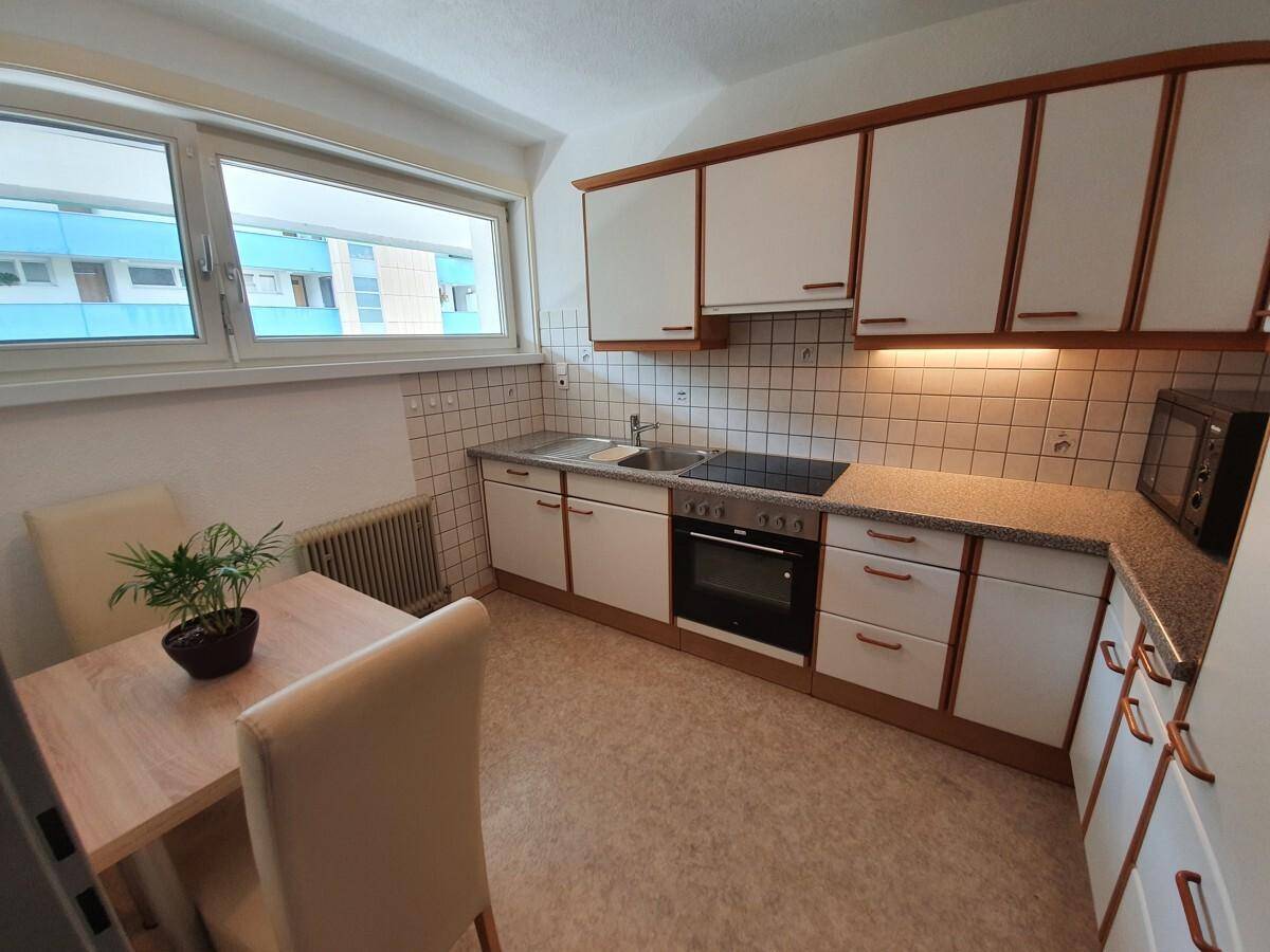 Helle Küche mit Fenster, weißen Schränken, integrierten Geräten und Essplatz für zwei Personen.