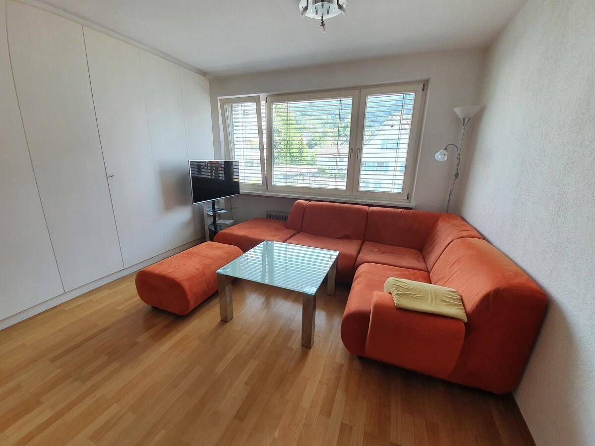 Helles Wohnzimmer mit orangefarbener Sitzecke, Holzboden und integriertem weißen Wandschrank.