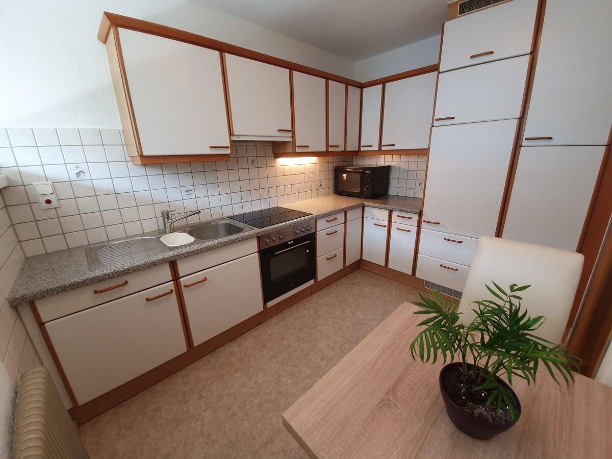 Funktionale Küche mit weißen Schränken, Holzdetails, Fliesenboden und kleinem Essbereich.