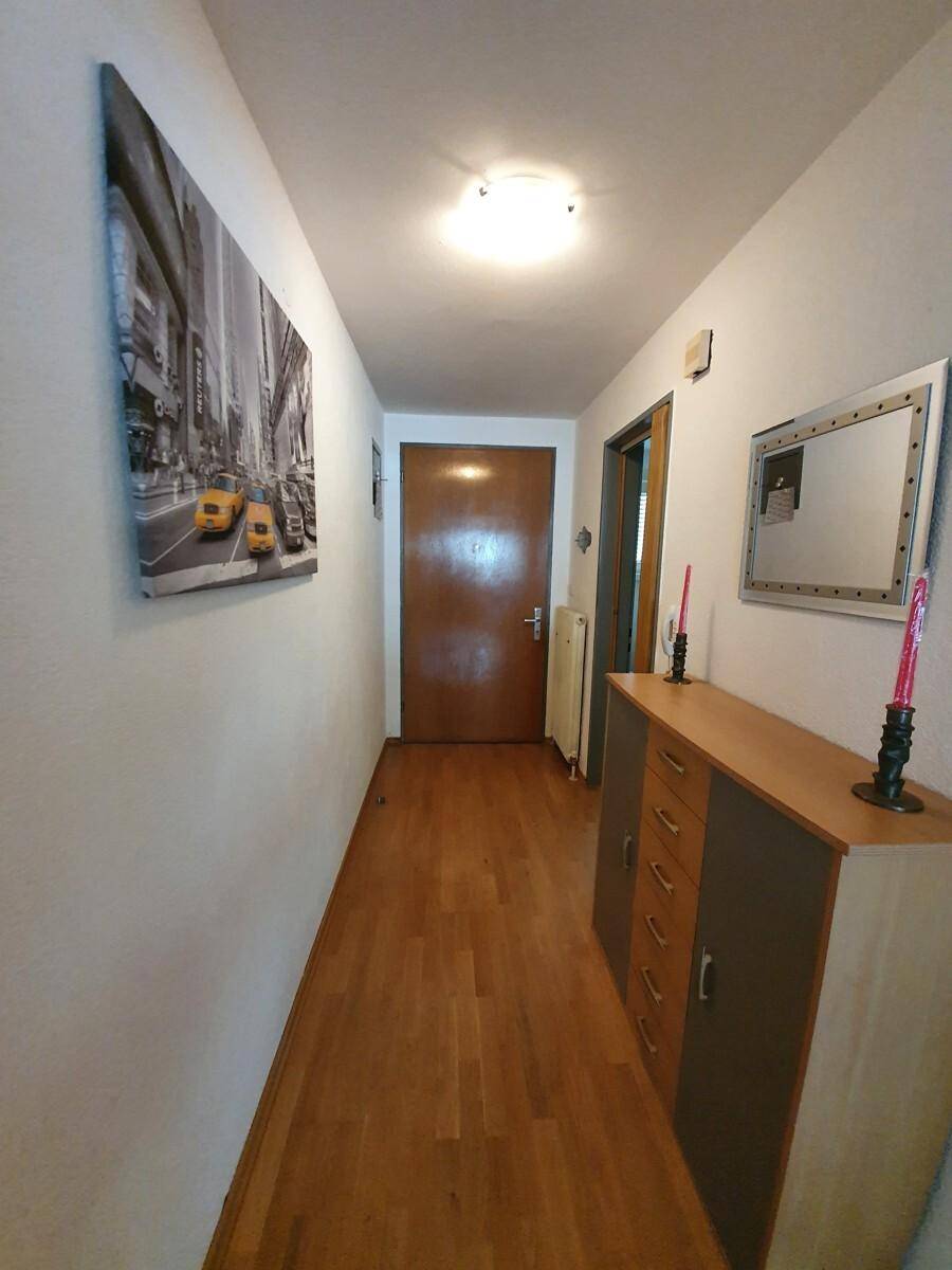Heller Flur mit Holzboden, einer Kommode und einem Spiegel, der zum Eingangsbereich führt.