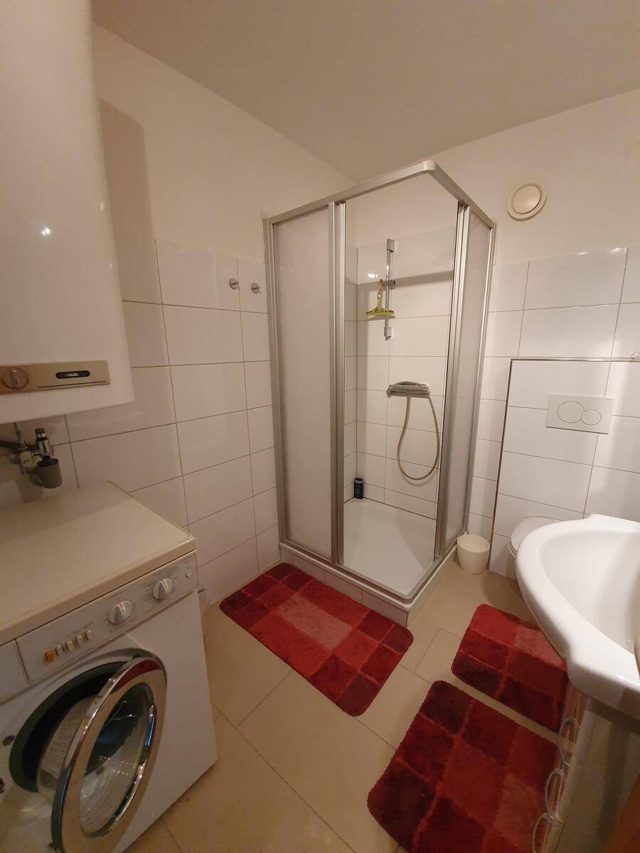 Kleines Badezimmer mit Duschkabine, WC, Waschbecken und Waschmaschine, komplett gefliest.