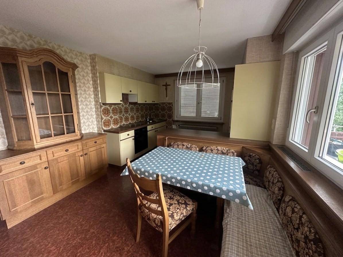 Traditionelle Wohnküche mit Essbereich, Holzmöbeln und gemusterter Tapete.