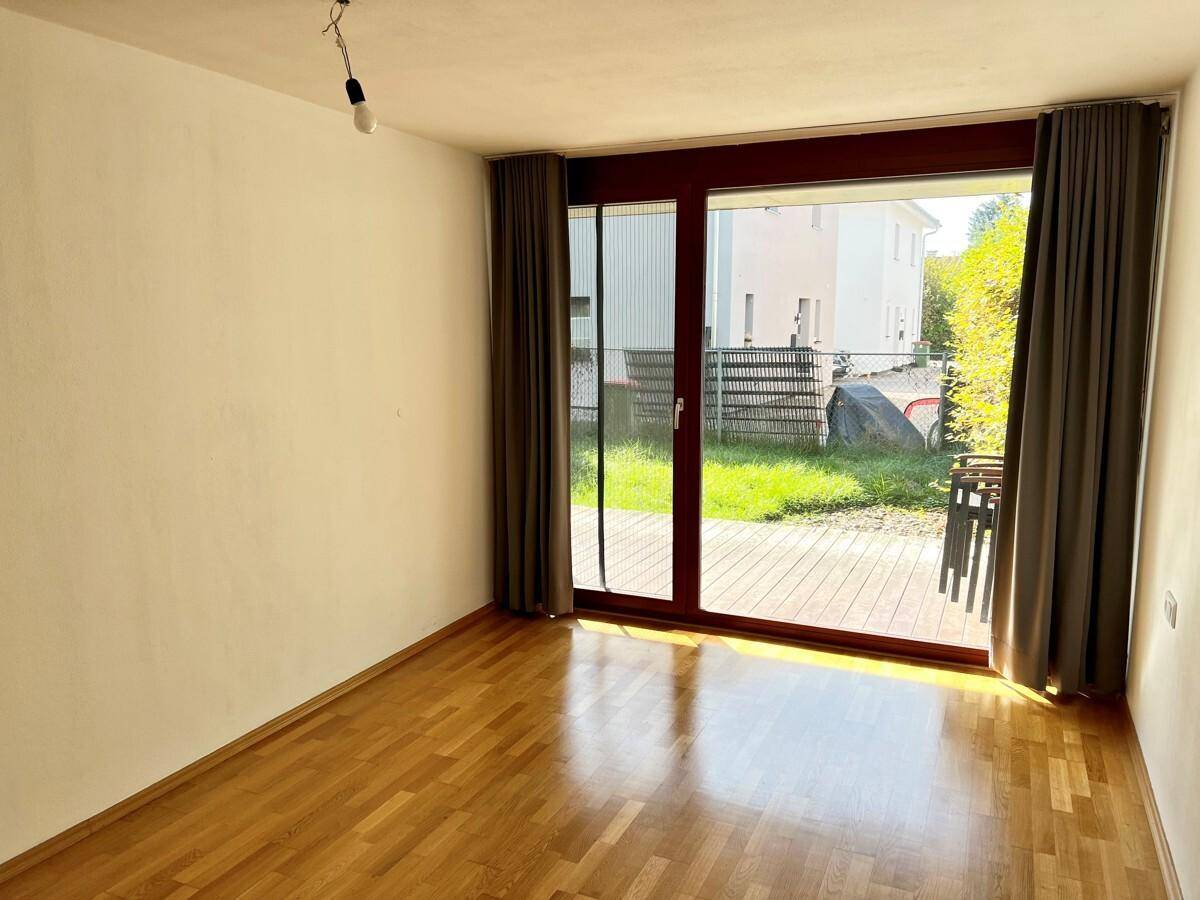 Geräumiger Raum mit Parkettboden und Zugang zu einer Terrasse oder einem Gartenbereich.