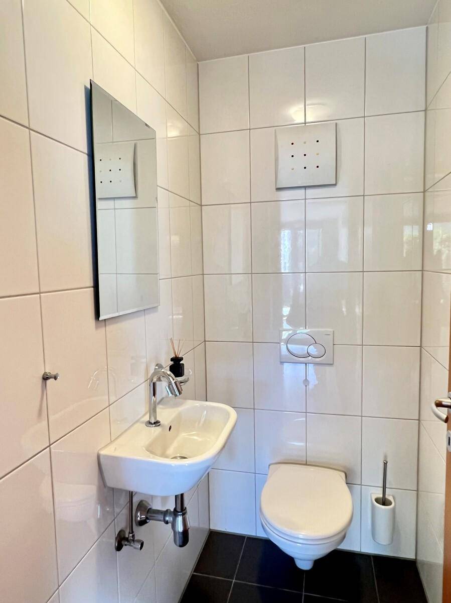 Kleines Gäste-WC mit wandhängender Toilette, Waschbecken und weißen Wandfliesen.